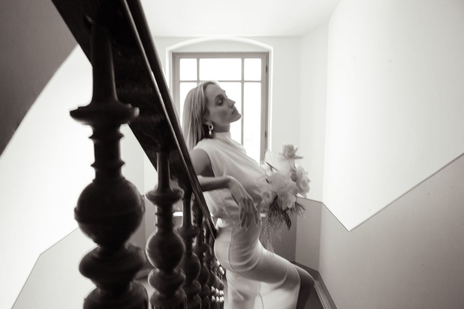 Black and white portrait of woman ascending staircase with bouquet.