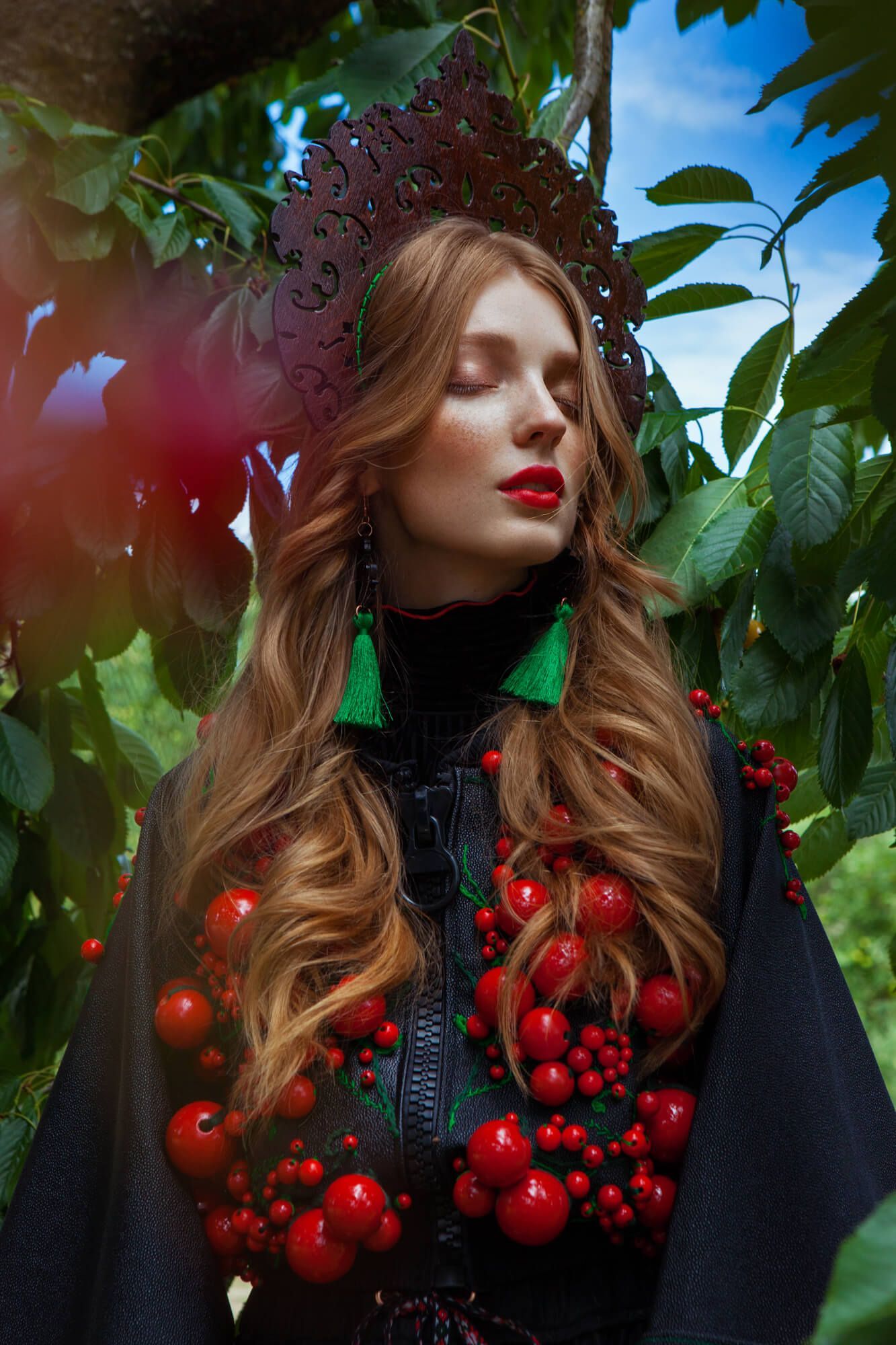 Autumn fashion portrait with crown of berries and dark clothing among green foliage.