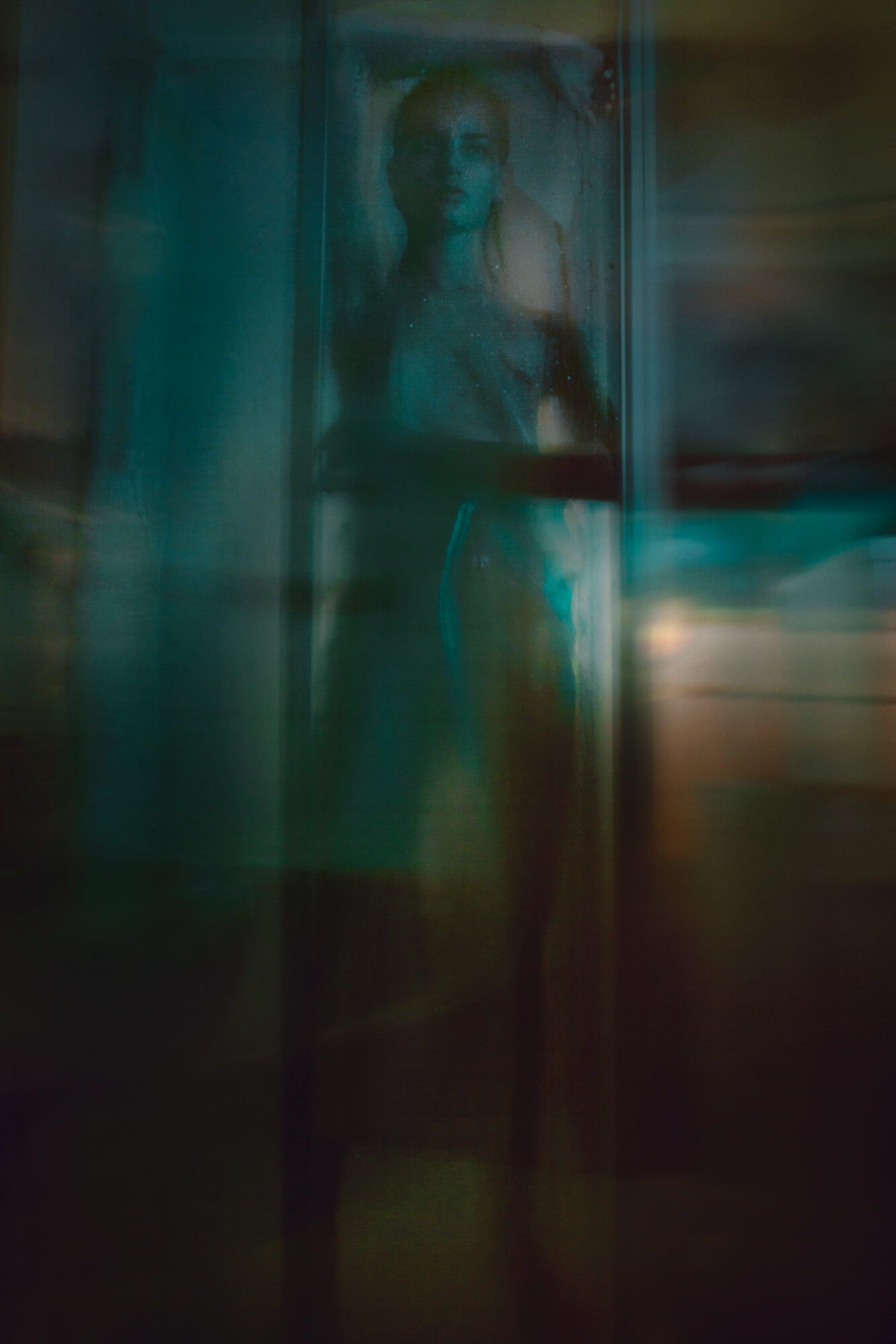 Ethereal silhouette behind glass with teal and amber lighting effects.