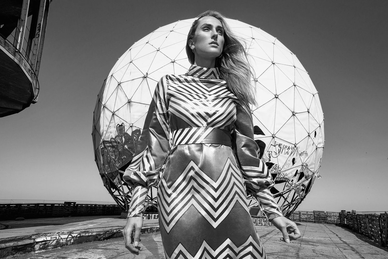 Fashion photo with model in zigzag dress against geodesic dome structure.