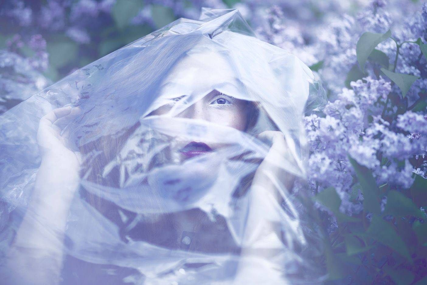 Dreamy portrait through sheer fabric with purple lilac flowers creating a soft ethereal mood.
