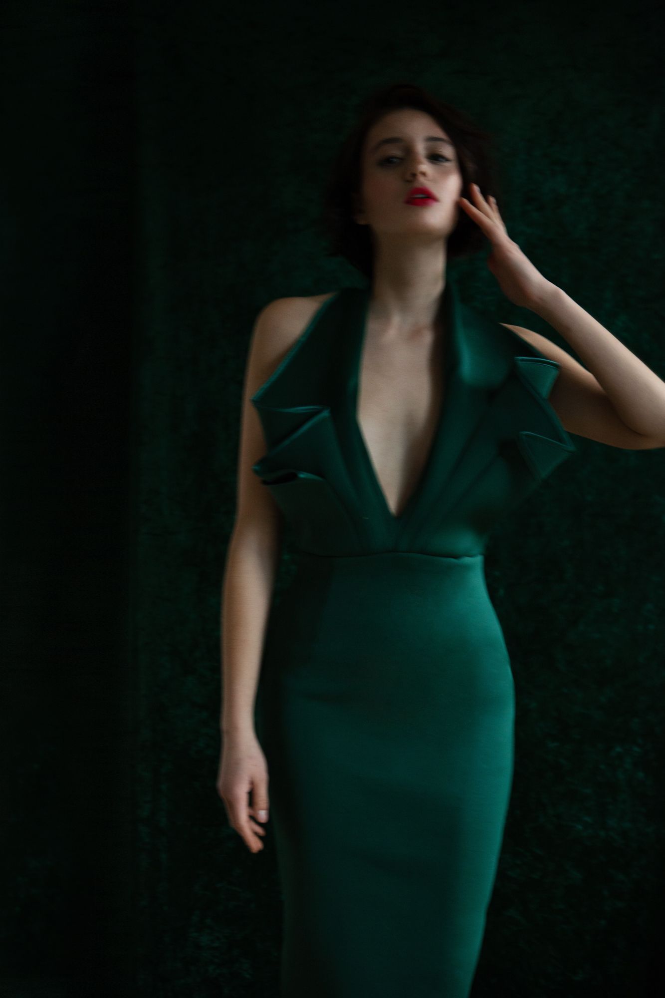 Elegant emerald green evening gown with plunging neckline photographed against dark background.