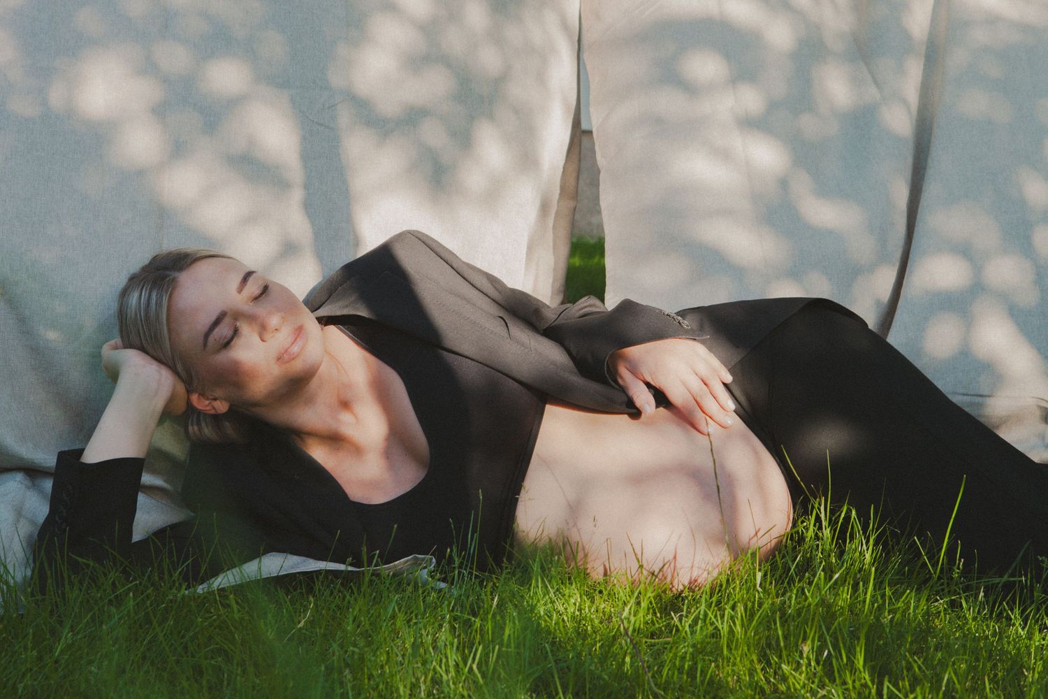 Maternity photo of figure resting on grass with dappled sunlight creating patterns.