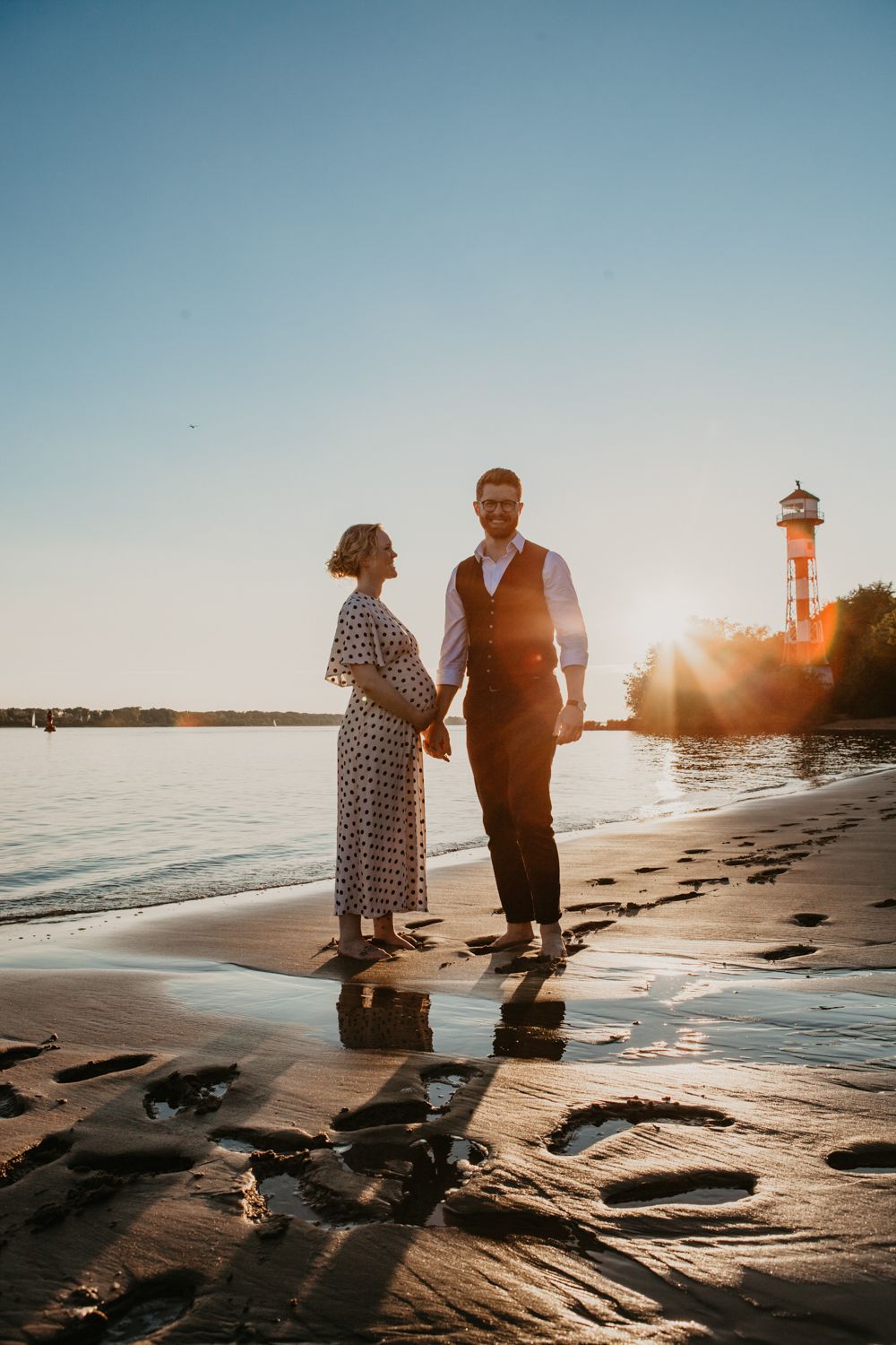 A romantic sunset beach scene with a couple silhouetted against the water near a lighthouse.