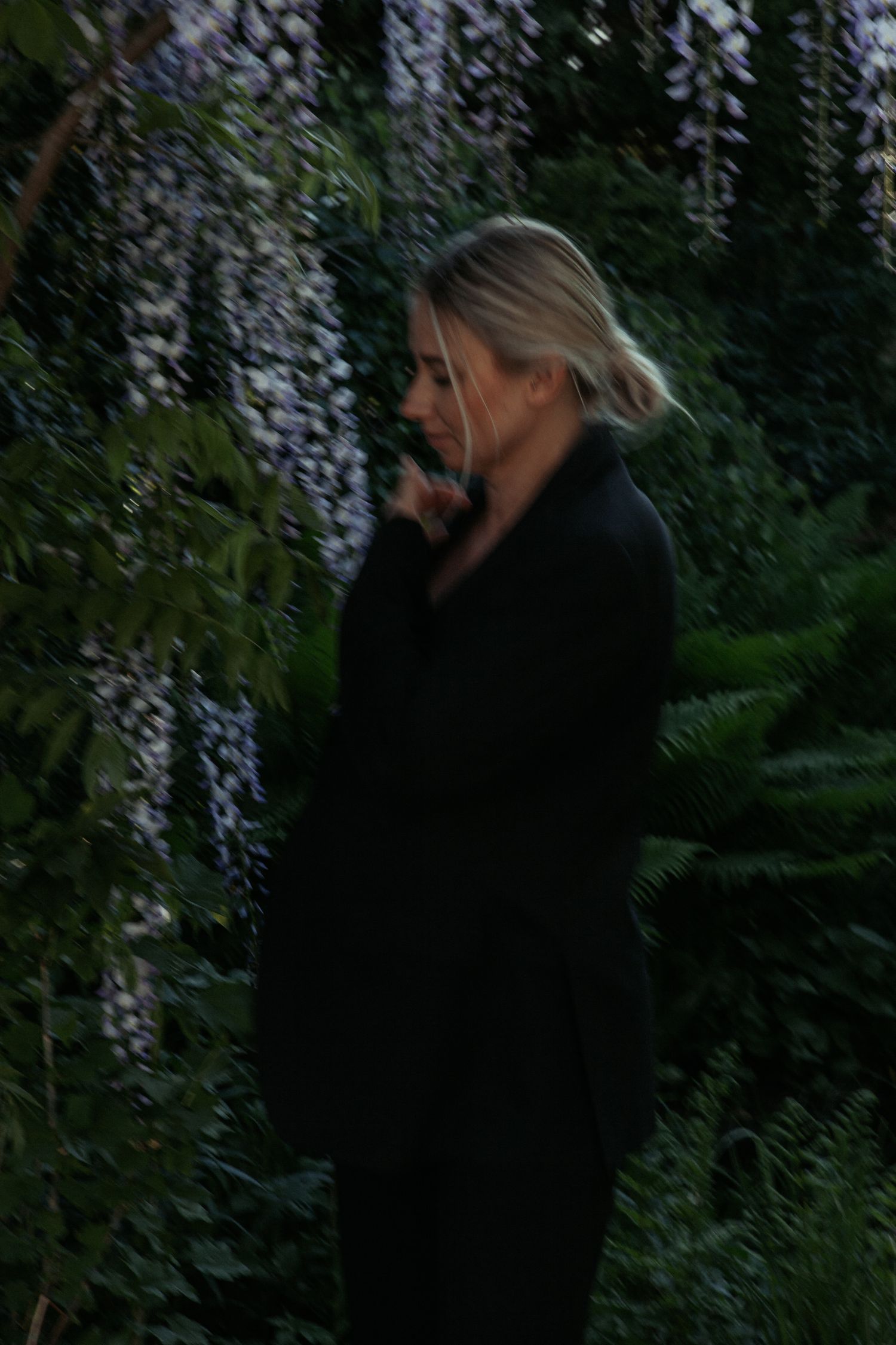 Moody evening portrait in a lush garden with cascading wisteria flowers.