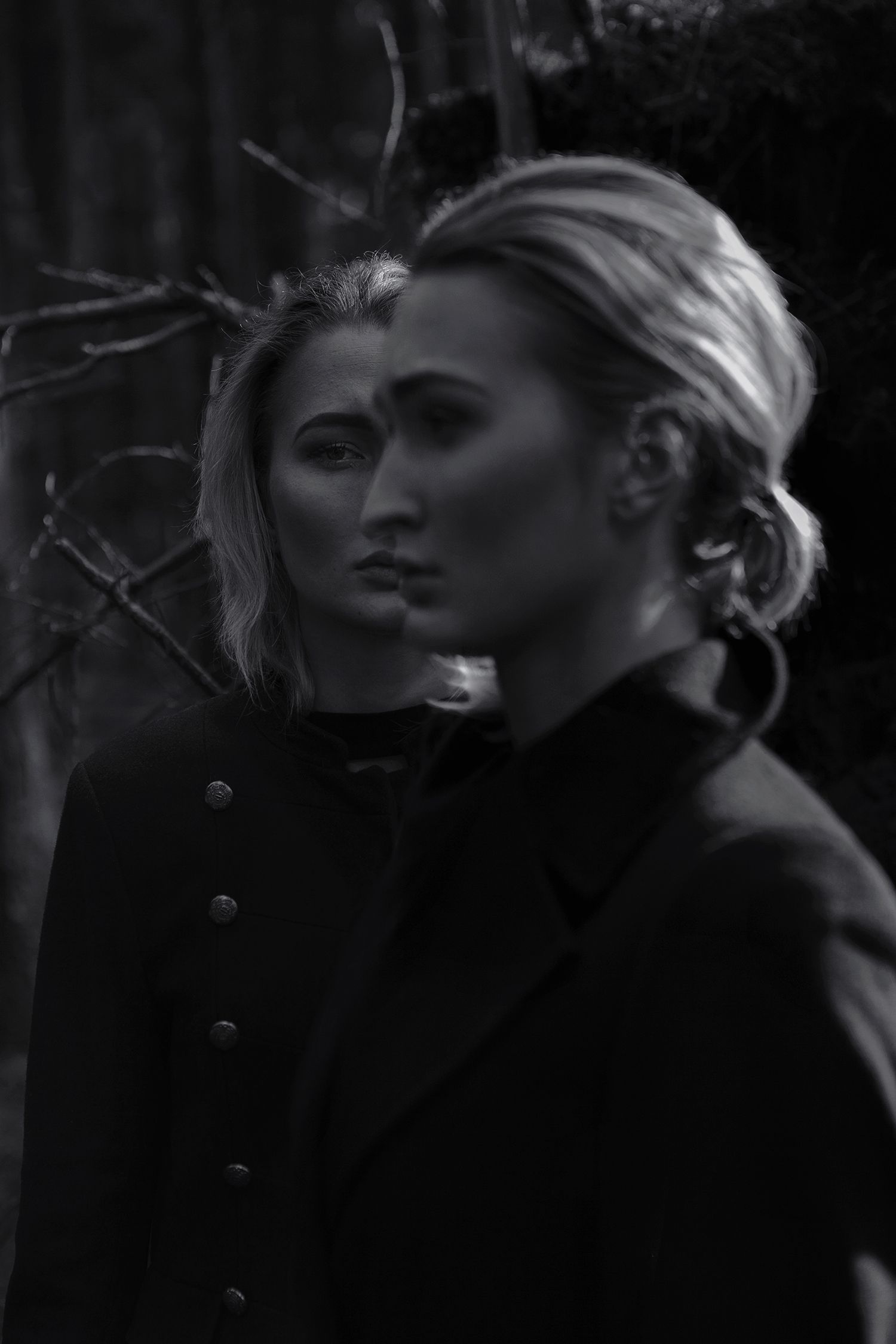 A close-up black and white portrait in a dark forest setting with dramatic lighting.