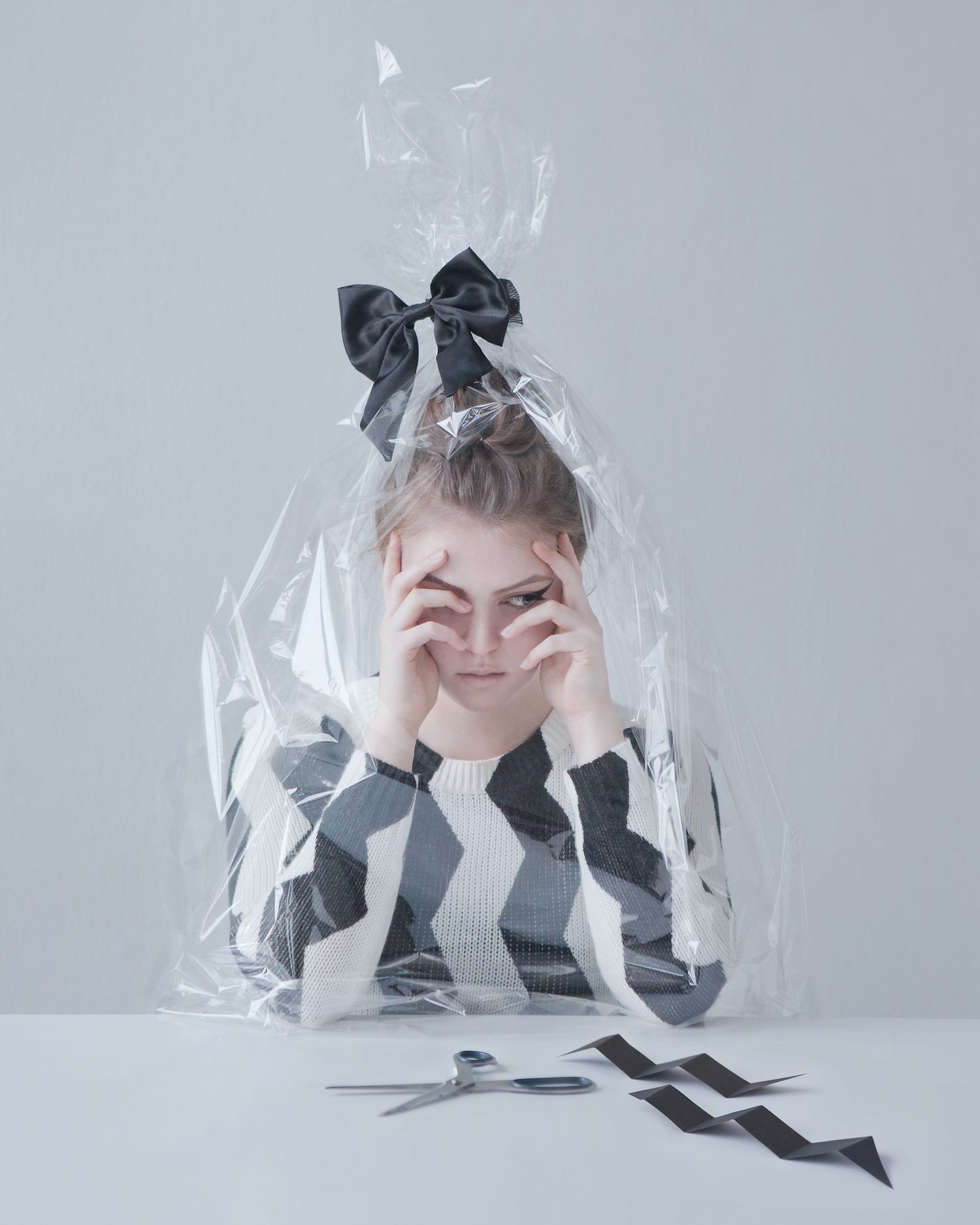 Whimsical portrait of a person wrapped in plastic with black bow wearing striped clothing.