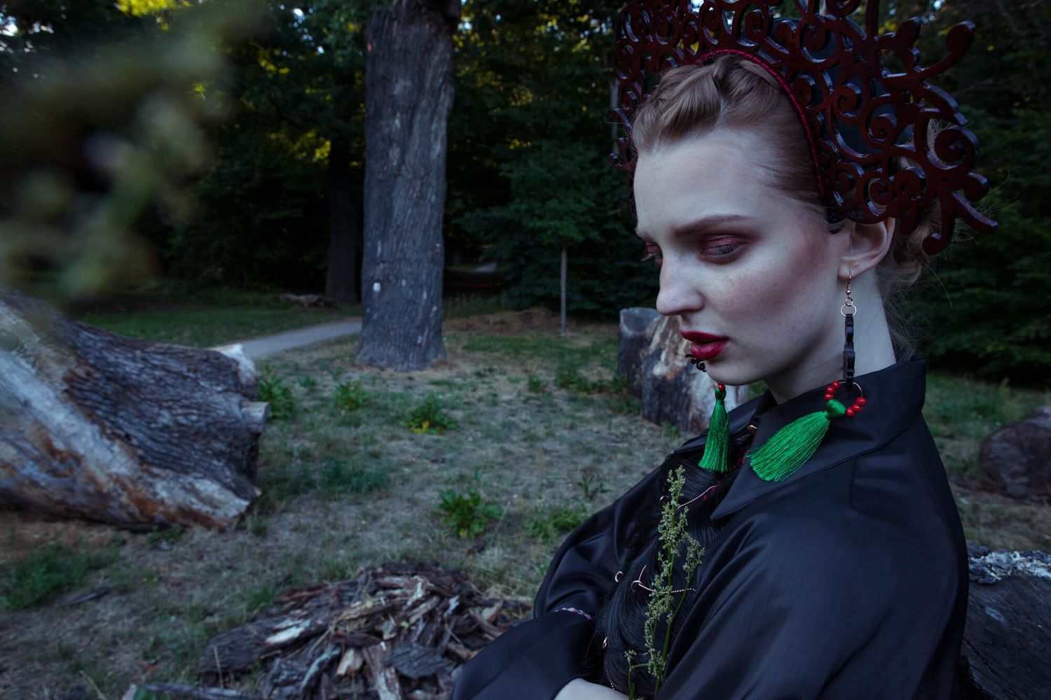 Moody fashion portrait with ornate headpiece and black attire in a forest setting.