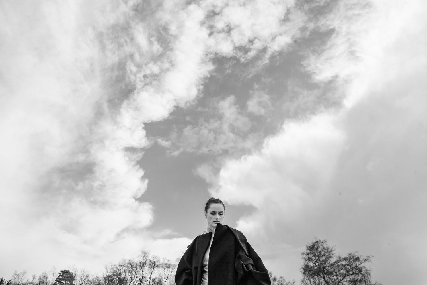 Dramatic low-angle fashion shot against cloudy sky in black and white.