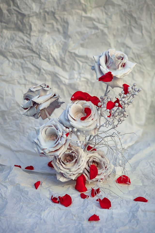 Elegant white roses with scattered red petals against textured paper background.