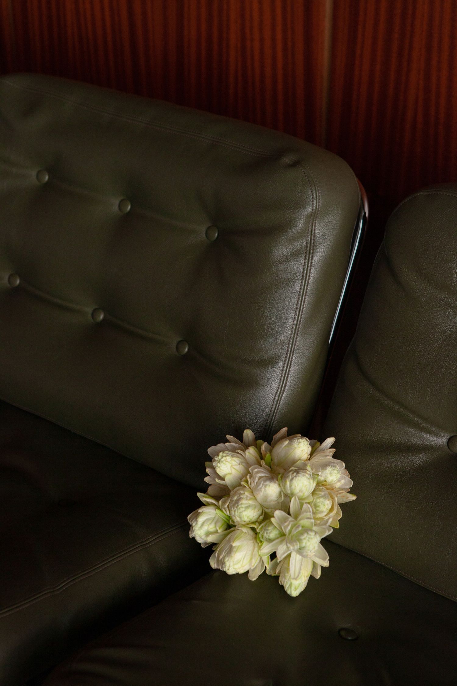 White tulip bouquet on dark green leather tufted couch in moody lighting.