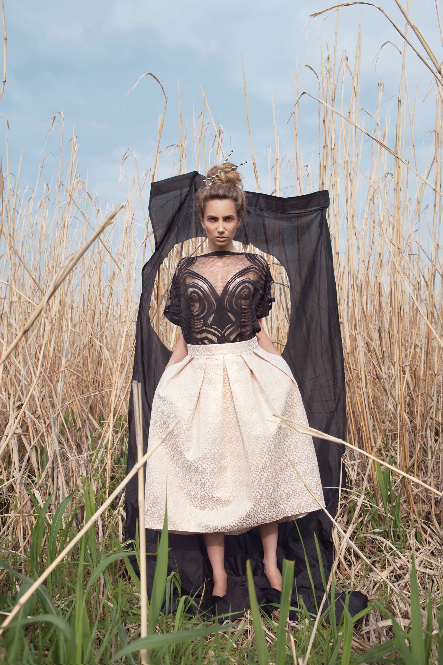Fashion scene in tall grass with black and white vintage-style dress and dramatic styling.