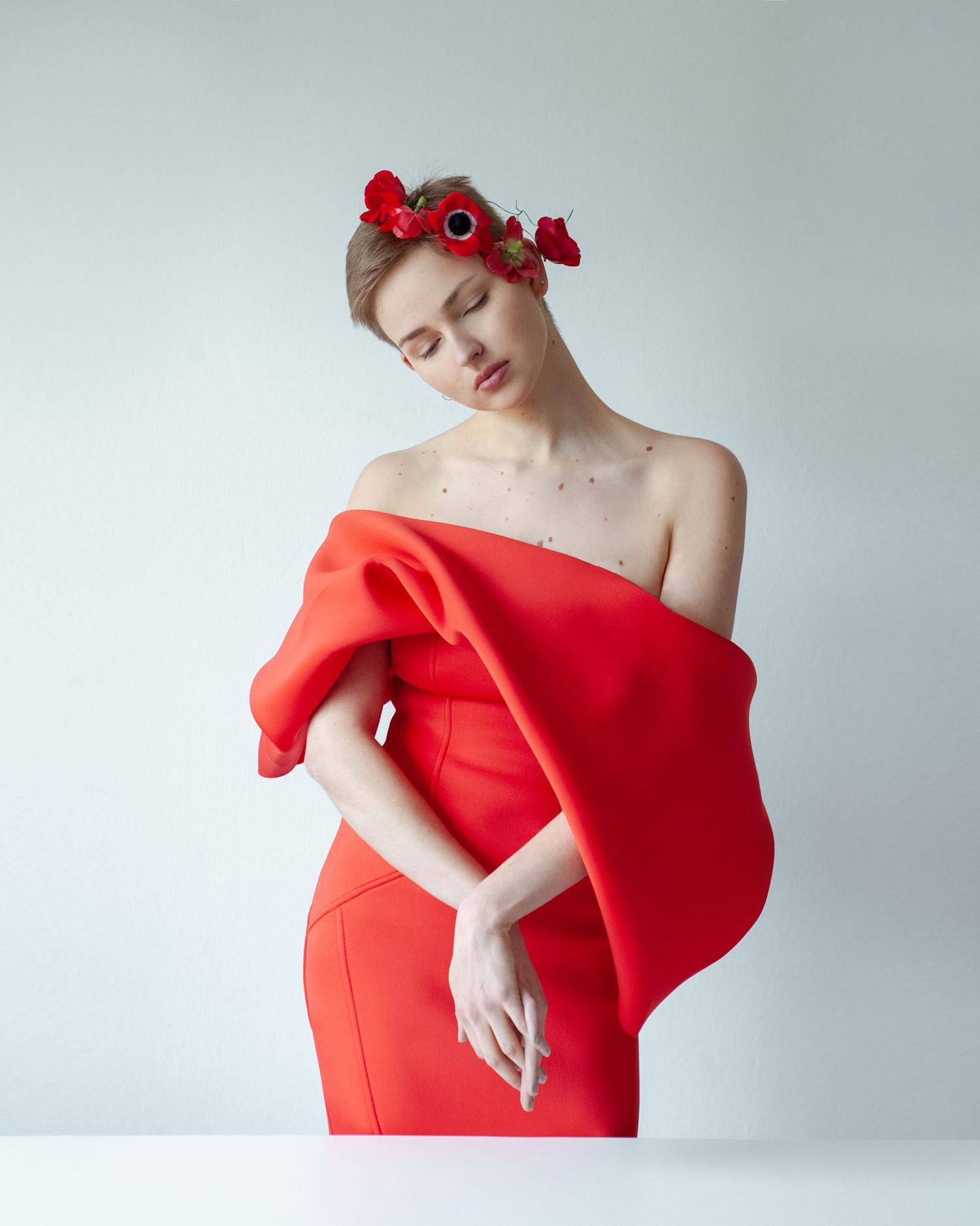 Fashion portrait featuring red dress and floral crown against minimal white background.