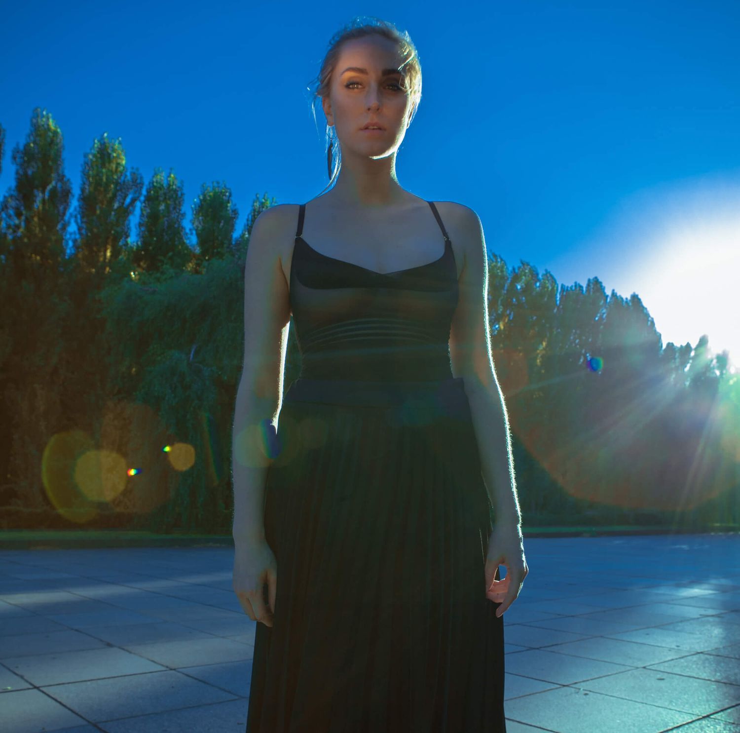 Silhouetted figure in black dress stands against blue twilight sky.