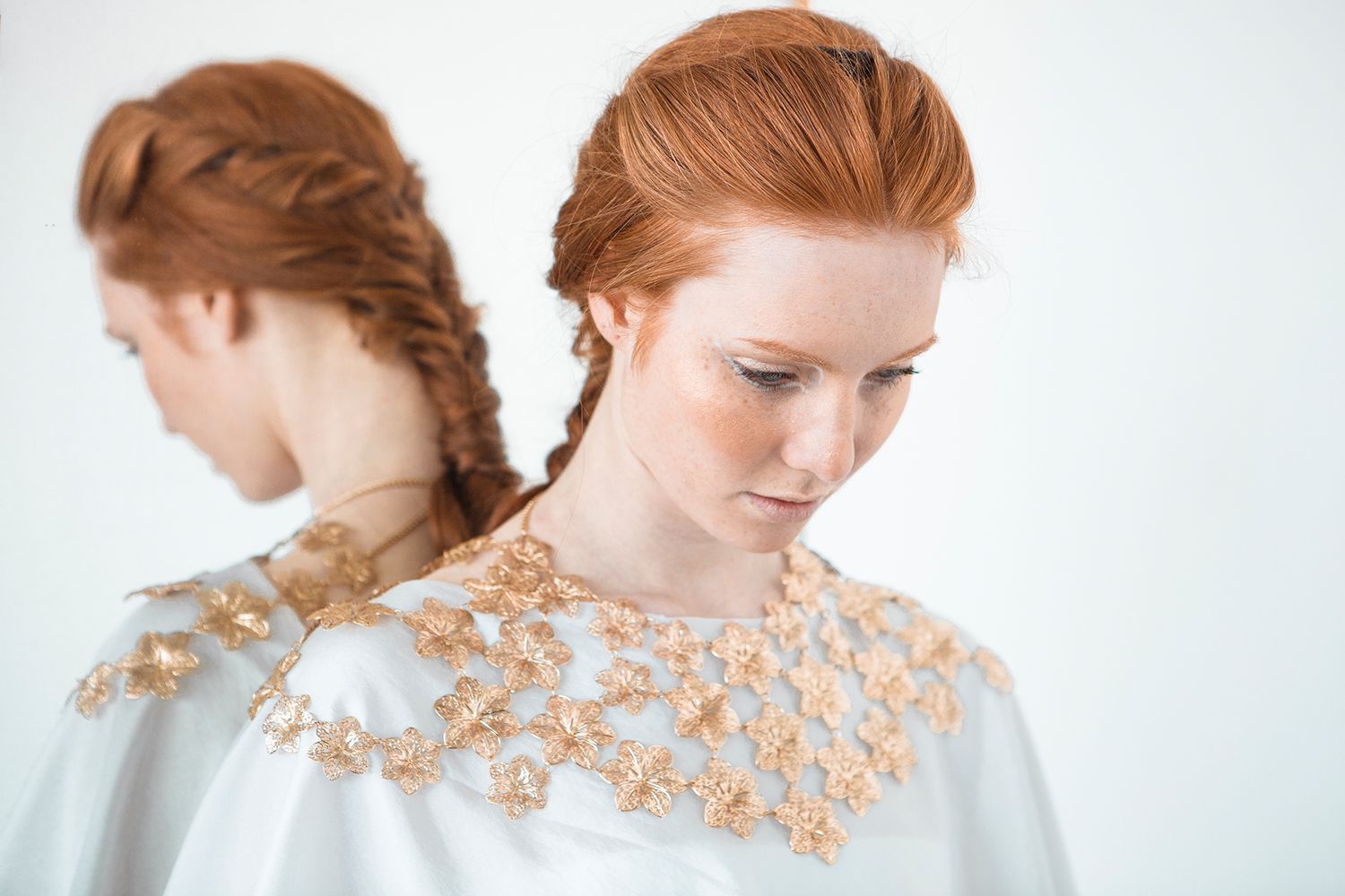 Figure wearing white dress adorned with gold metallic details in minimalist portrait.