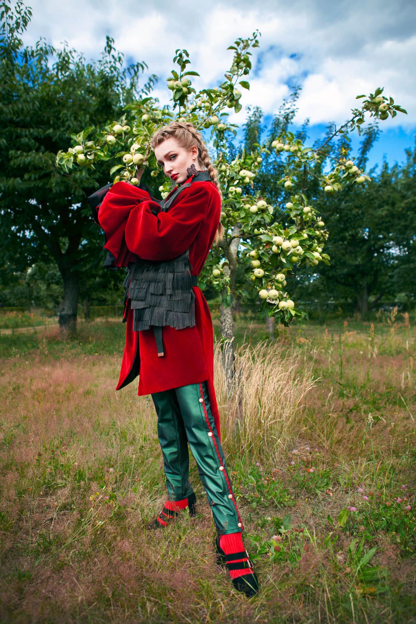 Avant-garde fashion styling with red coat and metallic pants in a rural field setting.