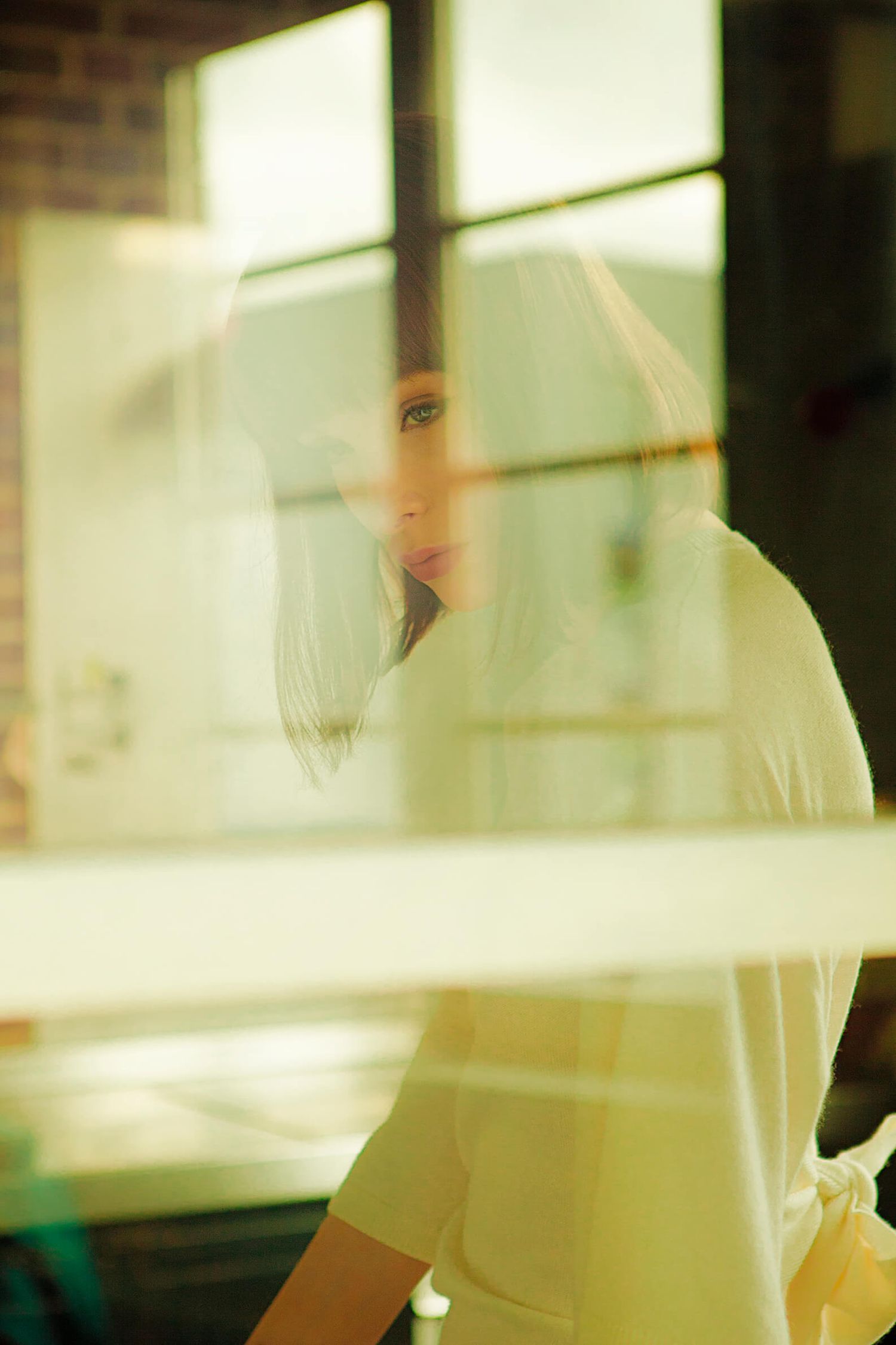 Soft focus portrait through window with golden light creating a dreamy vintage effect.