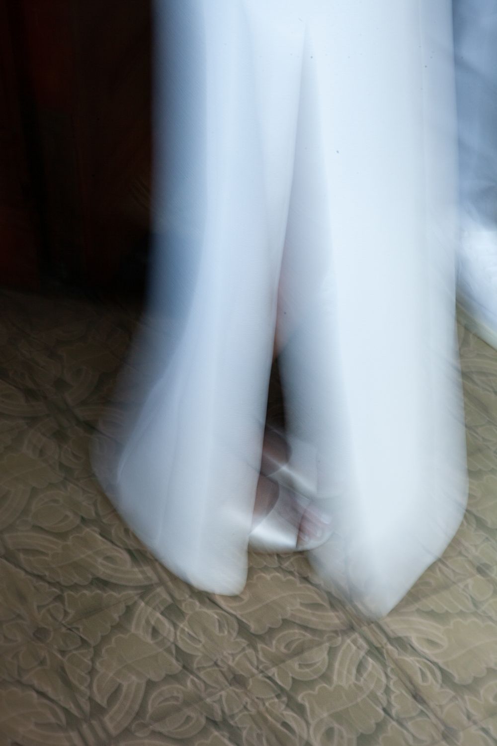 Blurred motion photograph showing white flowing fabric or dress against textured floor.