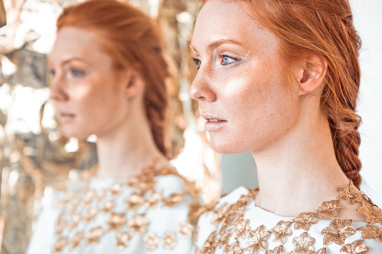 Mirrored portrait with gold embellished clothing against light background.