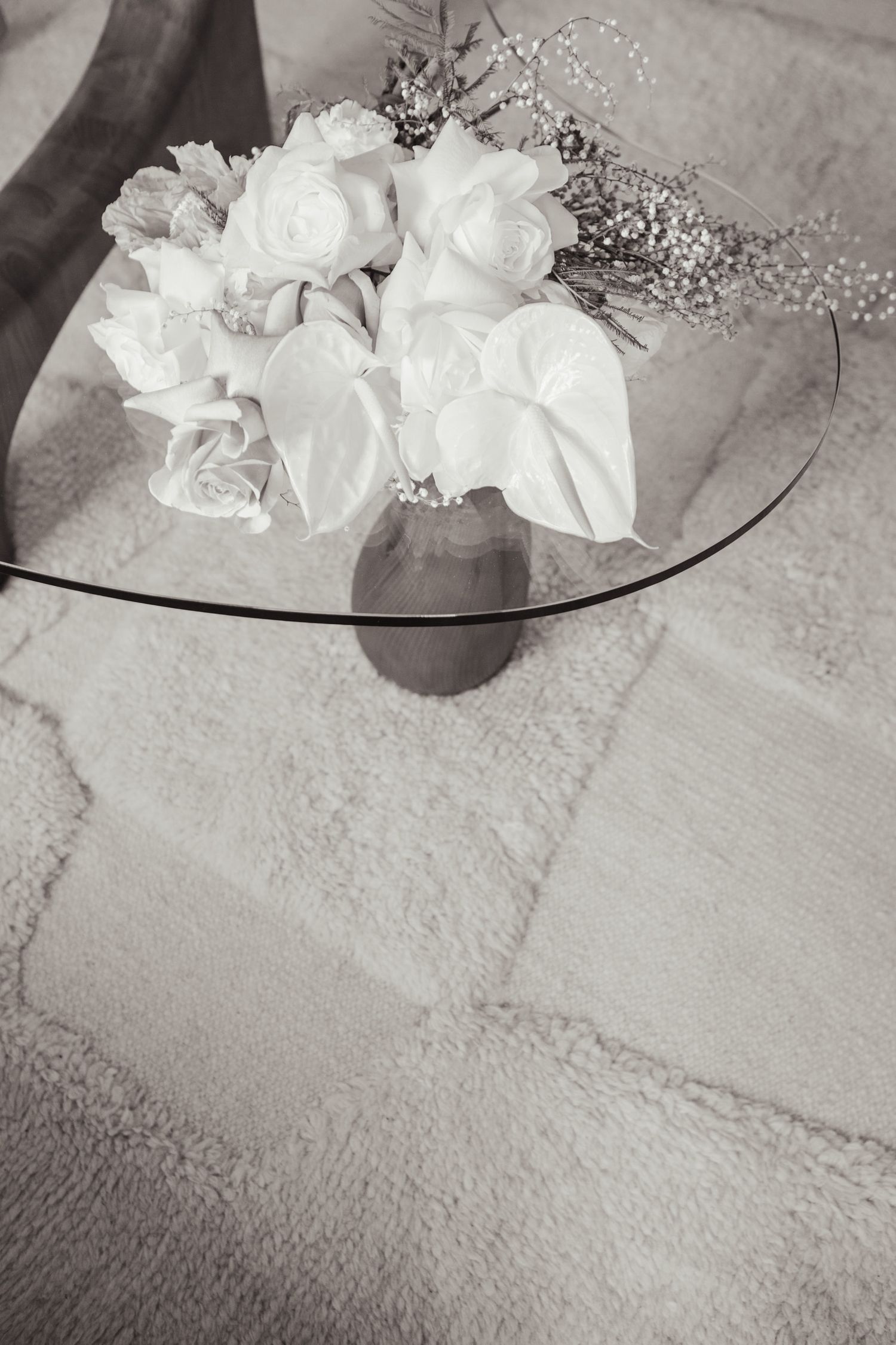 Black and white still life of white roses and baby's breath on glass table.