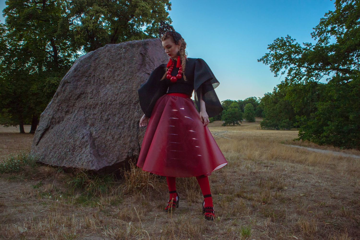 Artistic fashion photo featuring dramatic red skirt against rock formation in natural setting.