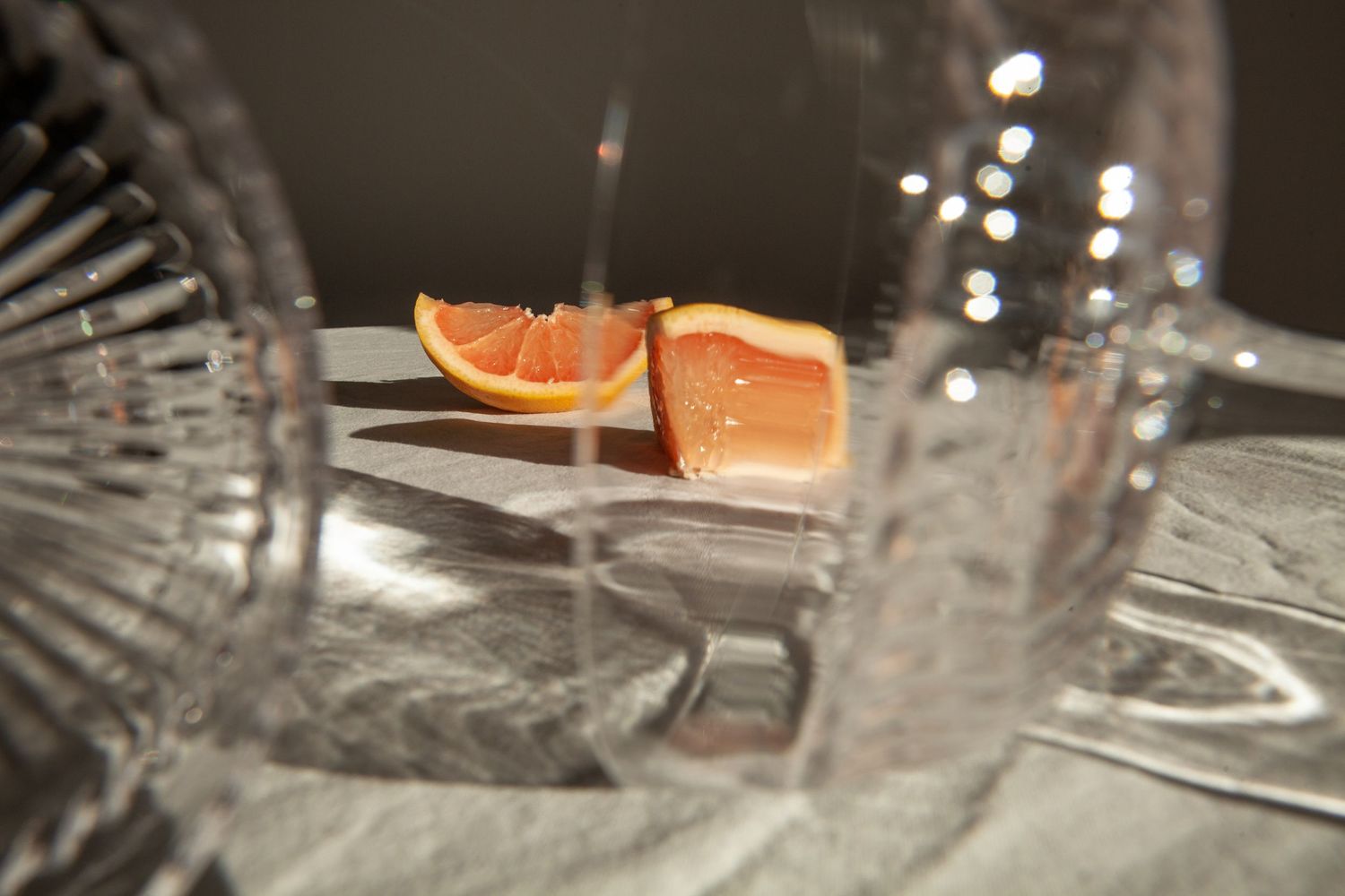 Sliced orange citrus segments on a reflective surface with crystal glassware in soft focus.