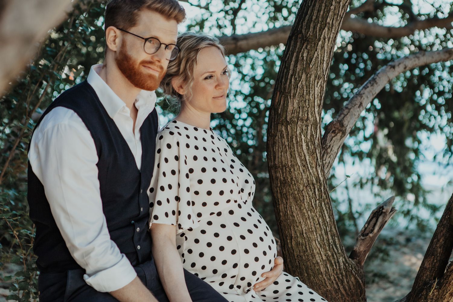 Couple in polka dot dress and vest pose against tree in outdoor setting.