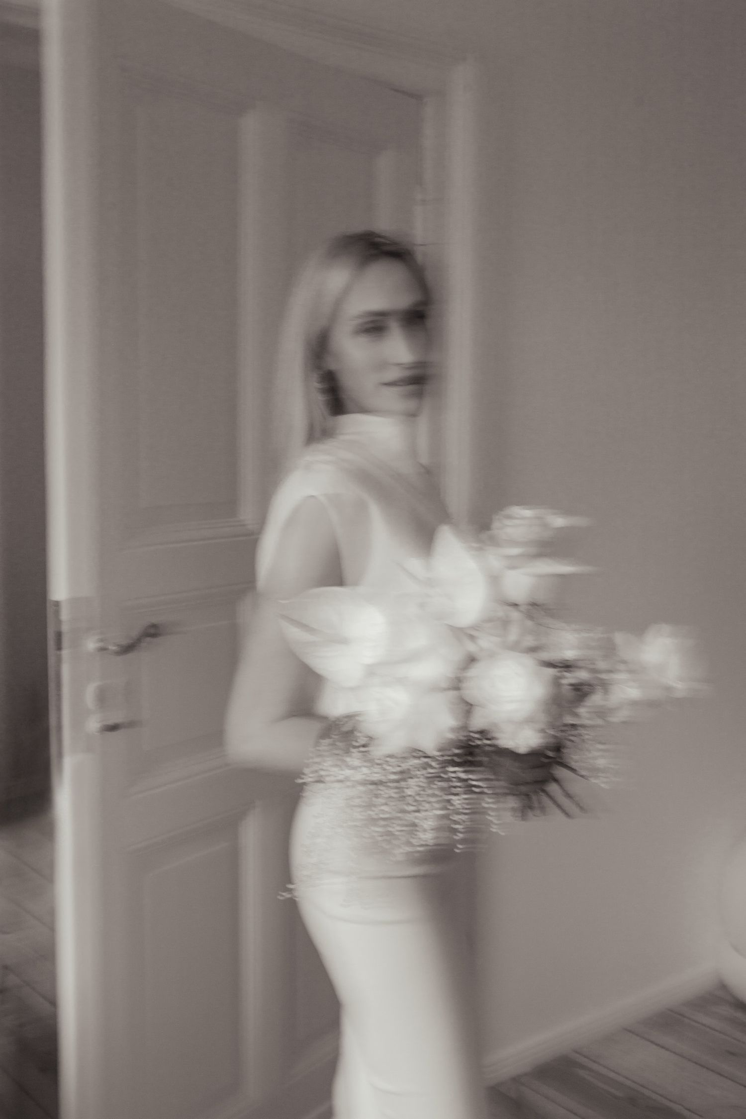 Artistic blurred black and white portrait of a bride holding a bouquet indoors.