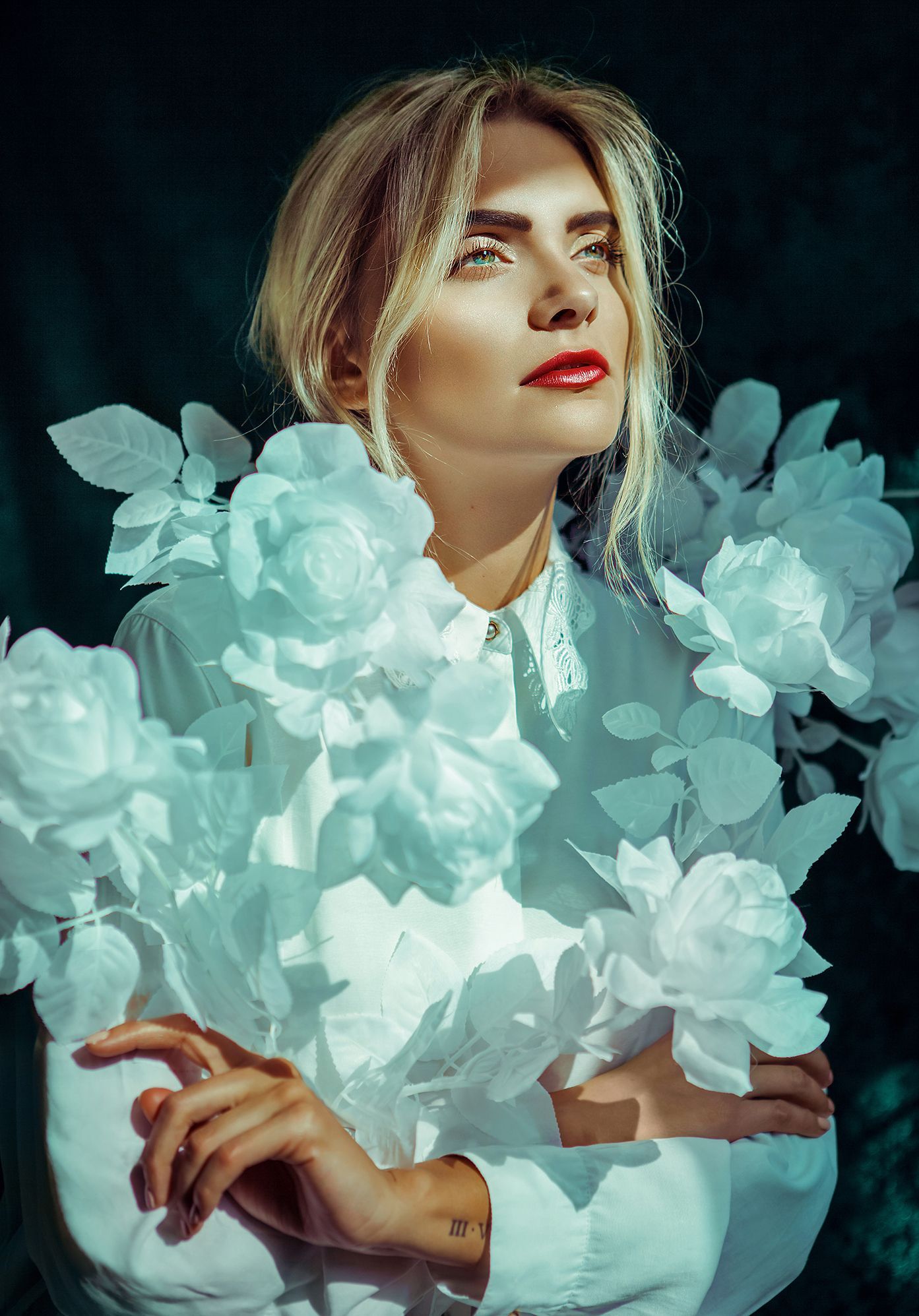 Ethereal portrait surrounded by glowing turquoise roses in dramatic lighting.