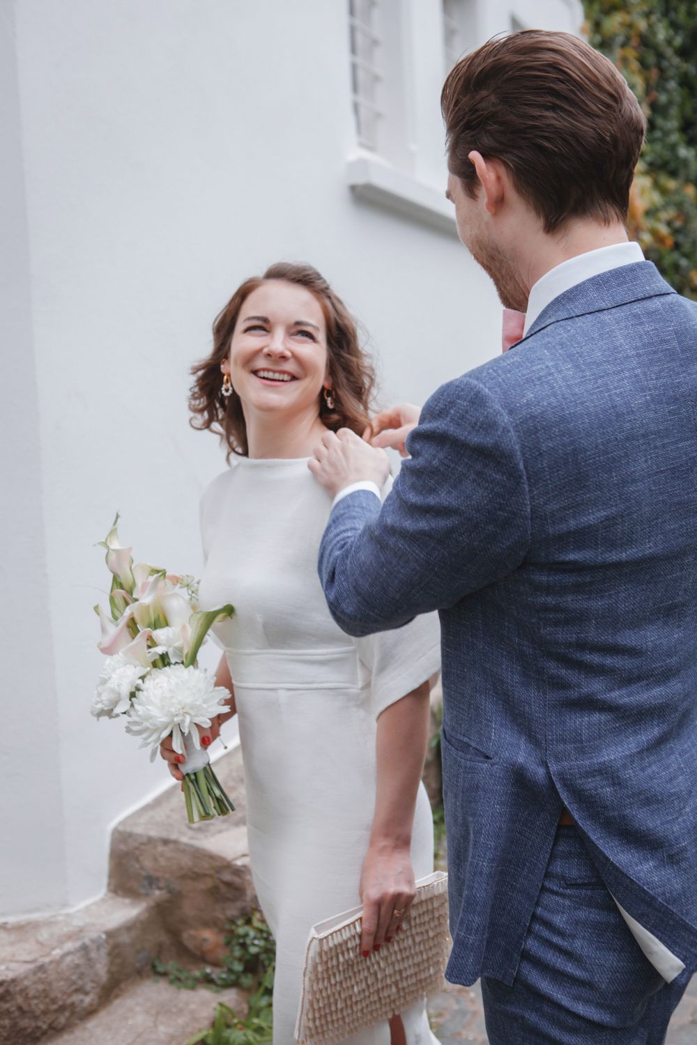 A romantic moment between a couple holding white flowers against a white wall during their wedding celebration.