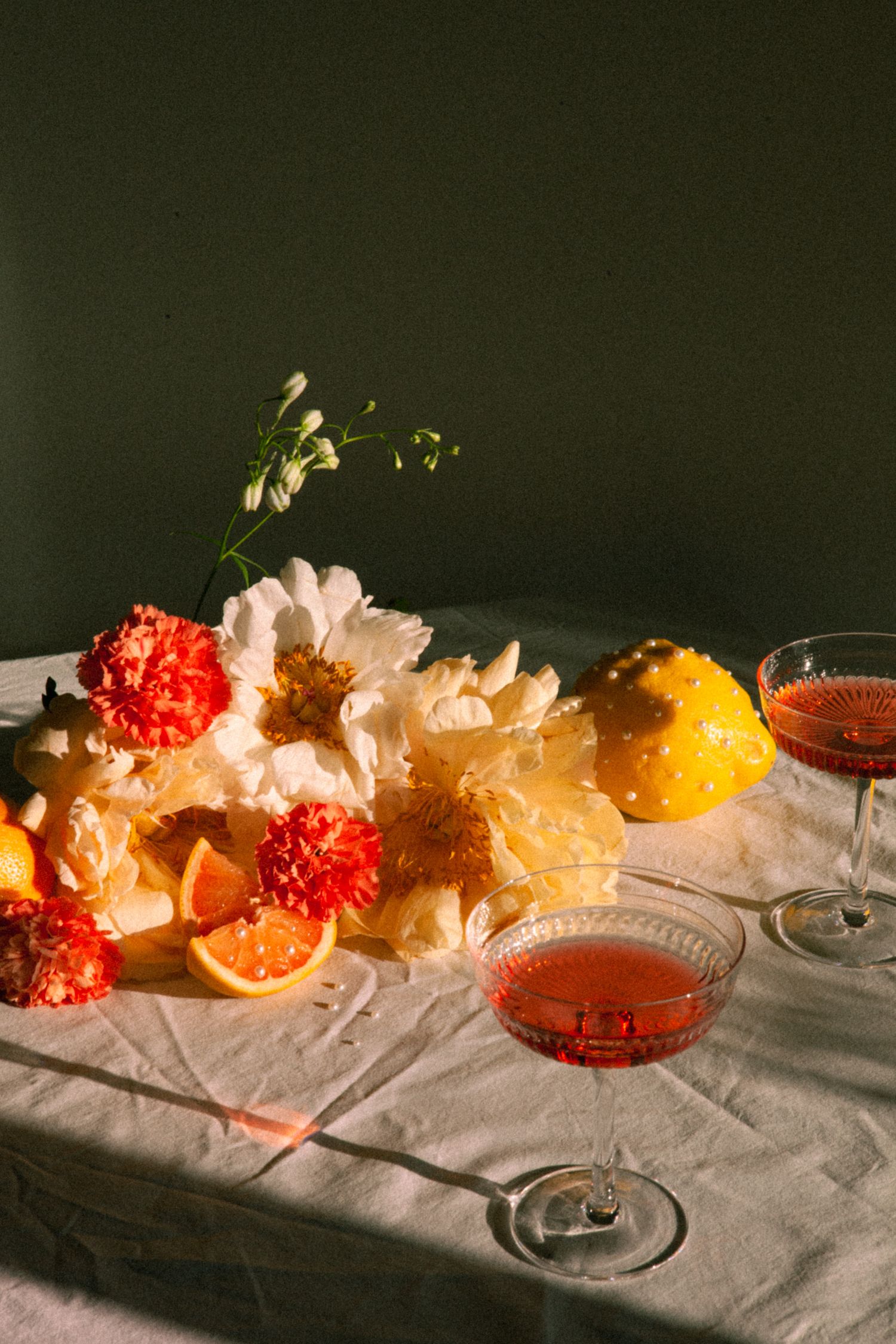 Elegant table setting with red cocktails, orange slices, and pink carnations in dramatic lighting.