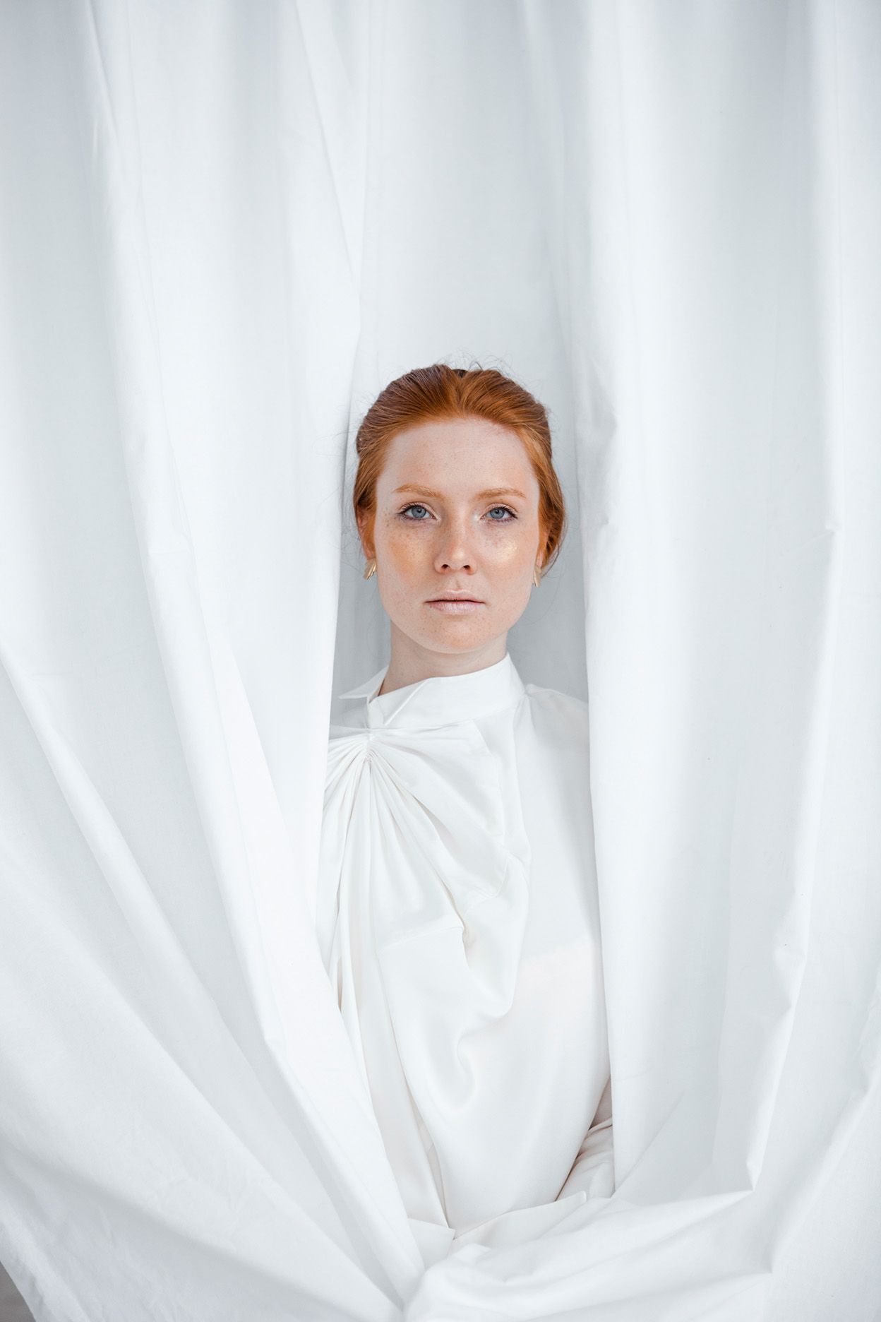 Figure in white clothing framed by flowing white curtains against minimal background.
