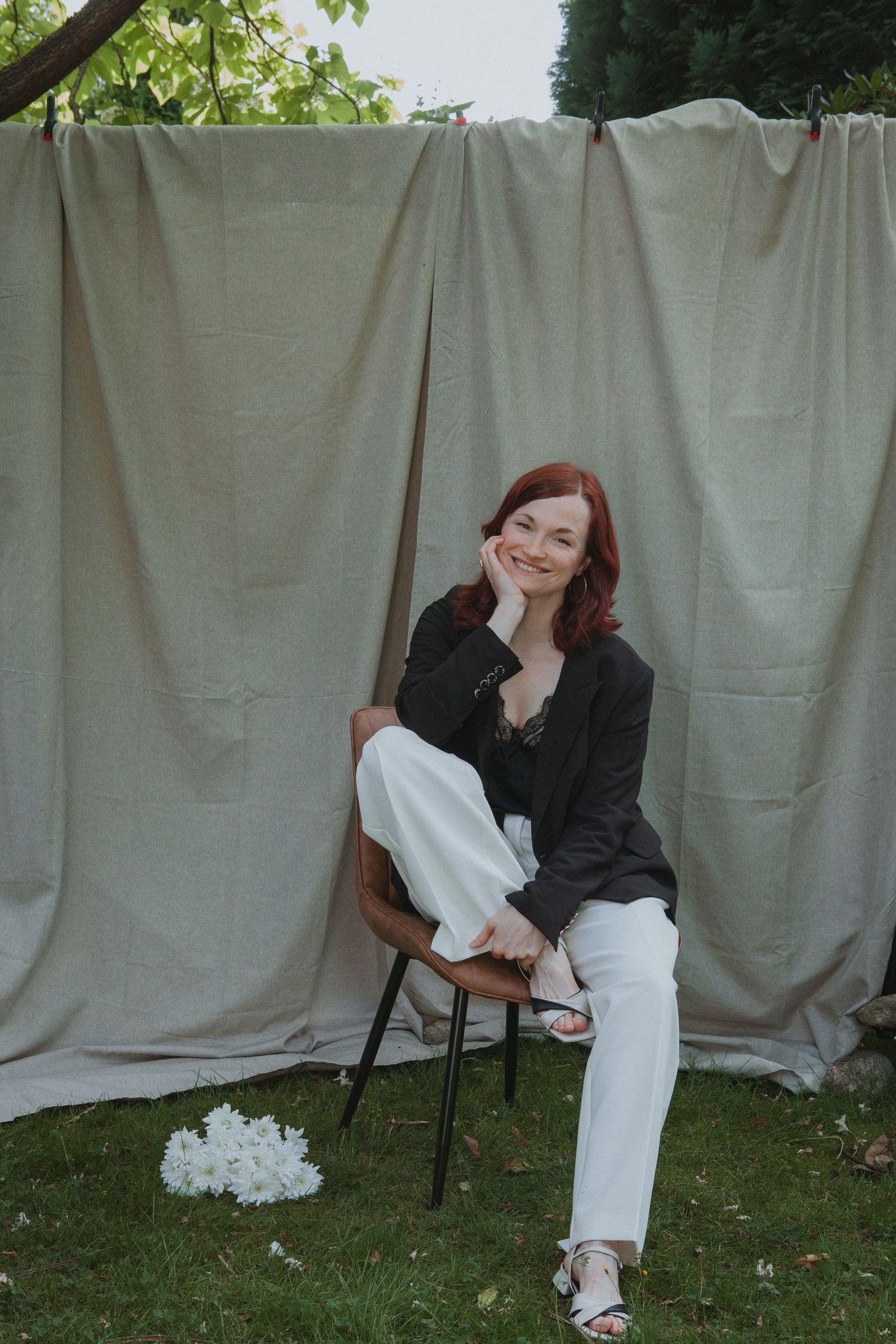 A casual portrait against a gray backdrop outdoors featuring white pants, black jacket and comfortable footwear.