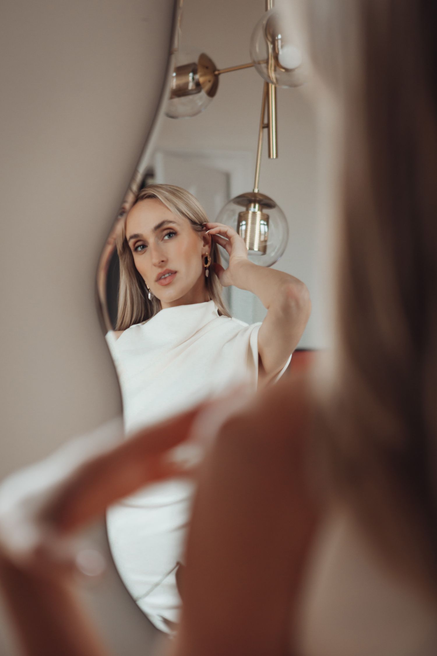 Artistic mirror reflection showing modern light fixture and elegant bridal styling.