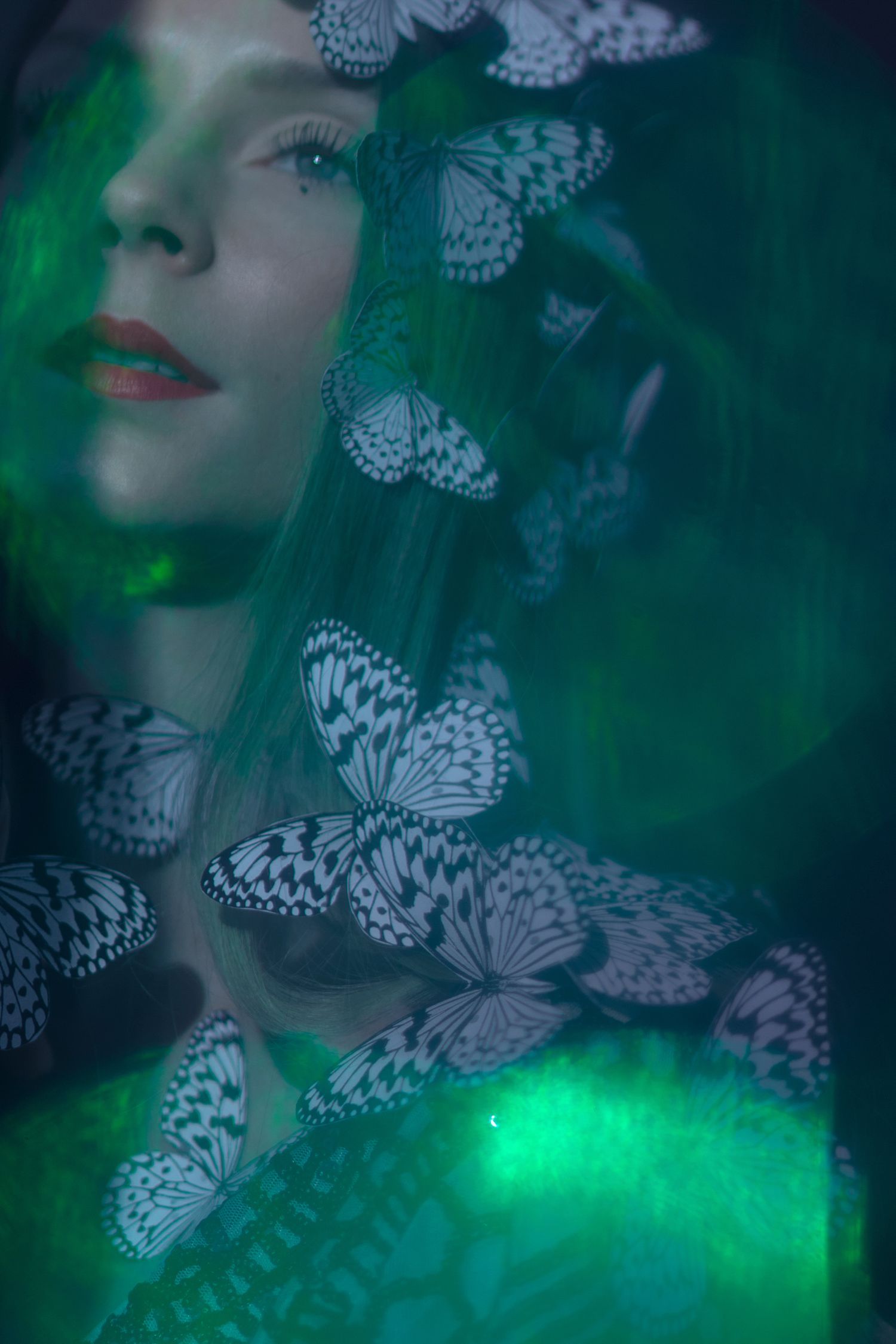 Ethereal portrait with white butterflies against emerald green background.