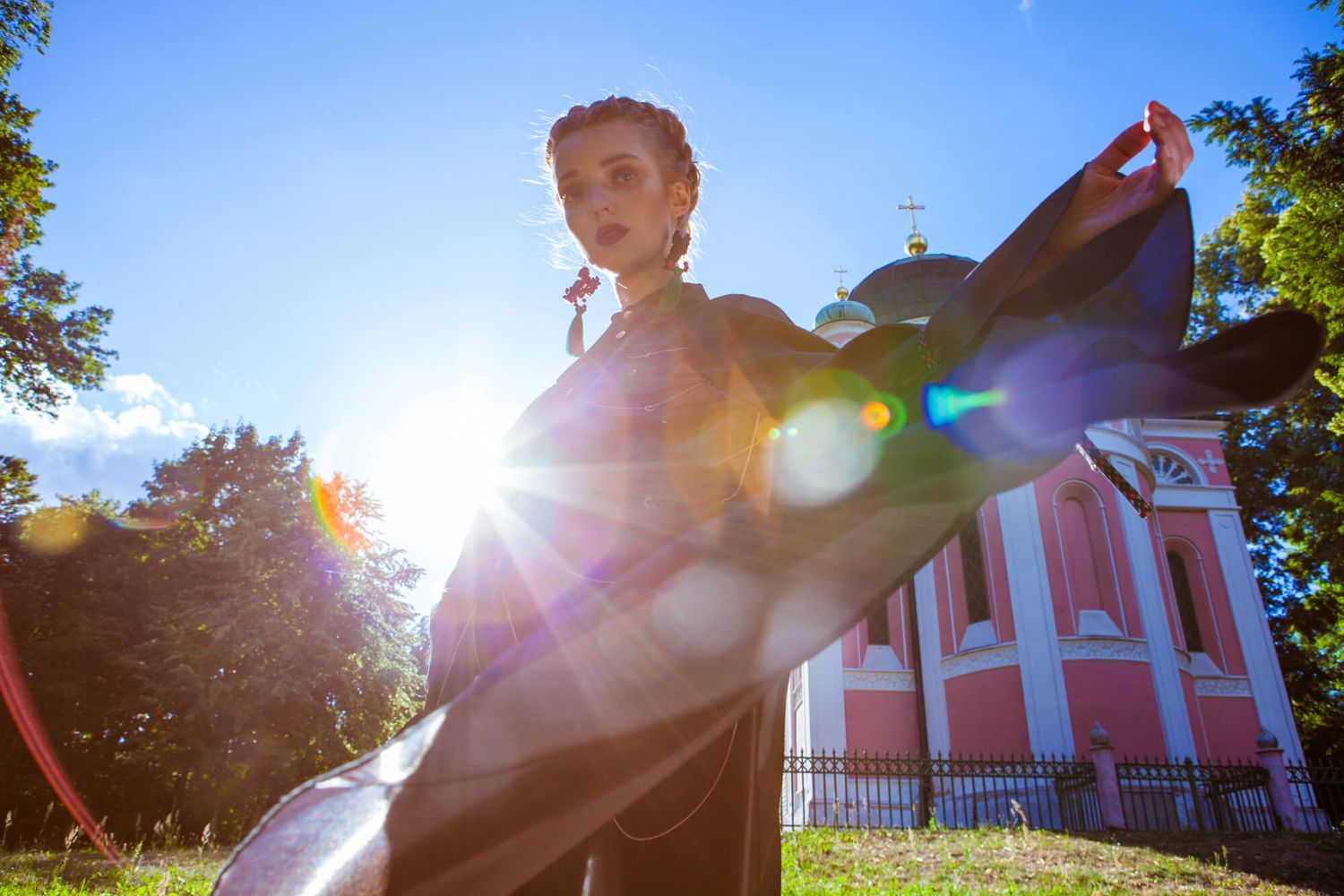 Dramatic backlit silhouette pose in front of a pink church building with sun flare effects.