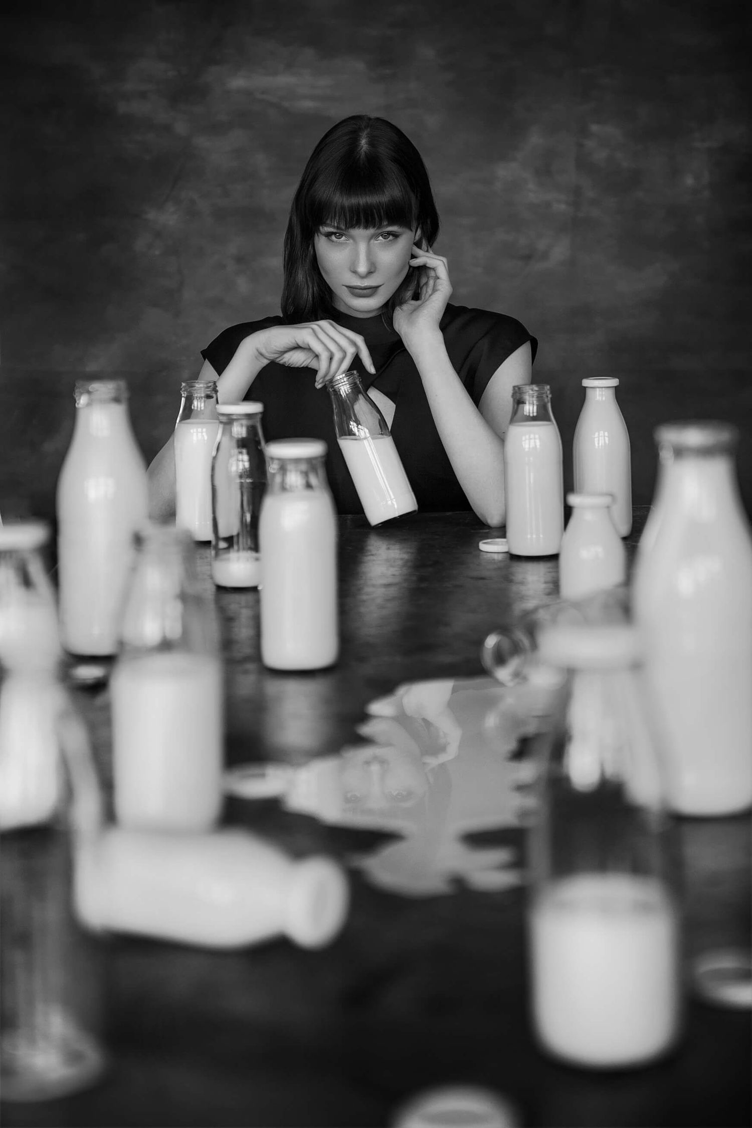 Moody black and white portrait with collection of milk bottles on dark wooden table.