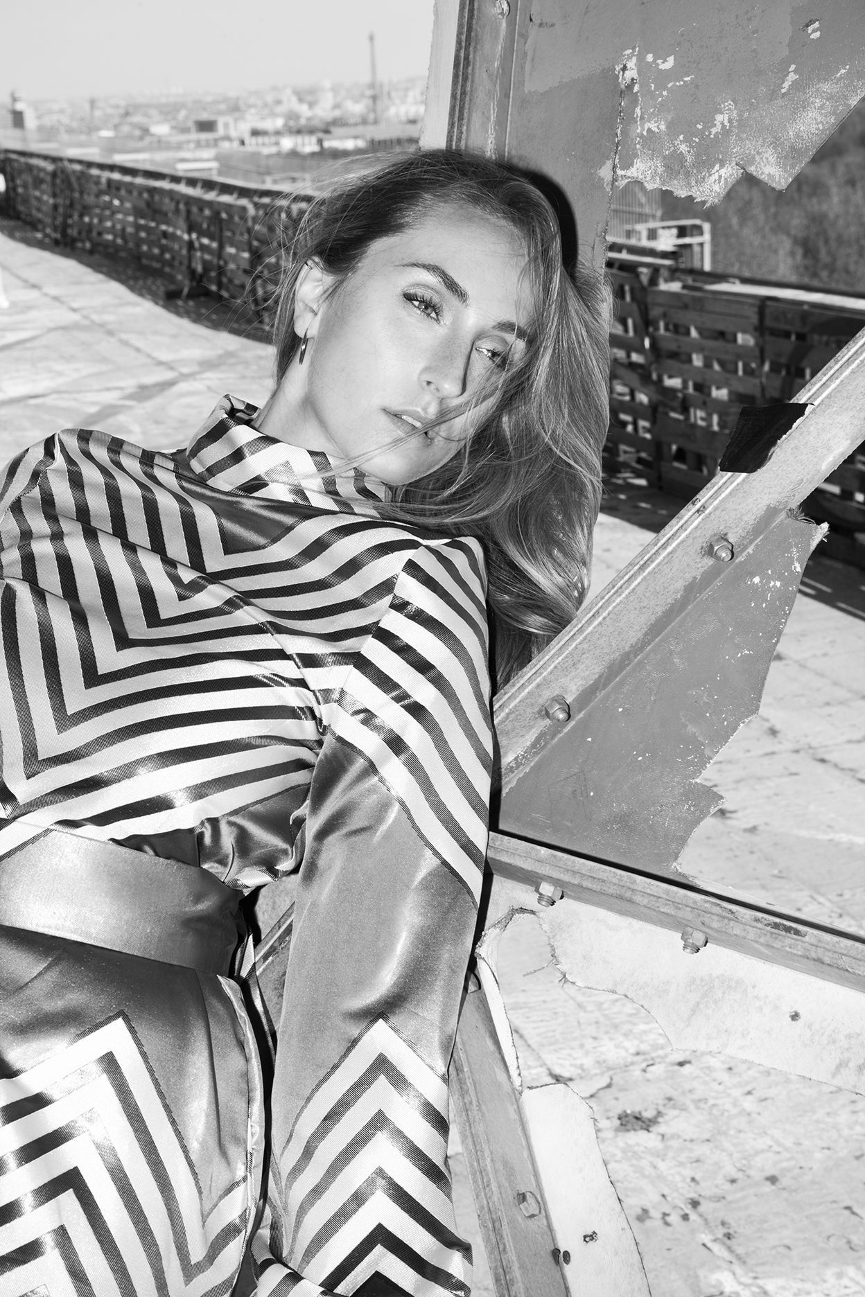 Black and white portrait of person in chevron pattern dress lounging on urban rooftop.