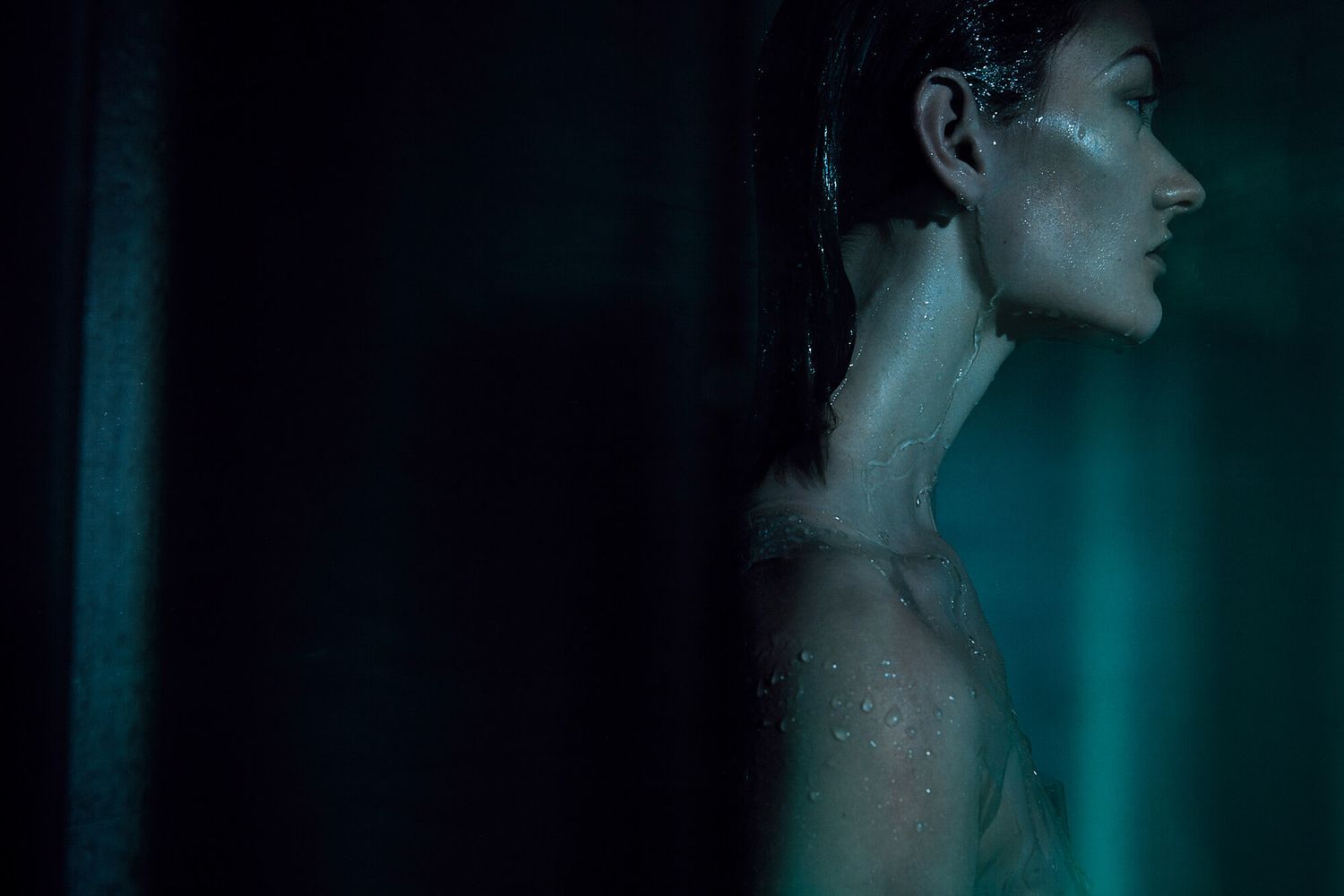 Artistic side profile portrait with drops of water in turquoise lighting.