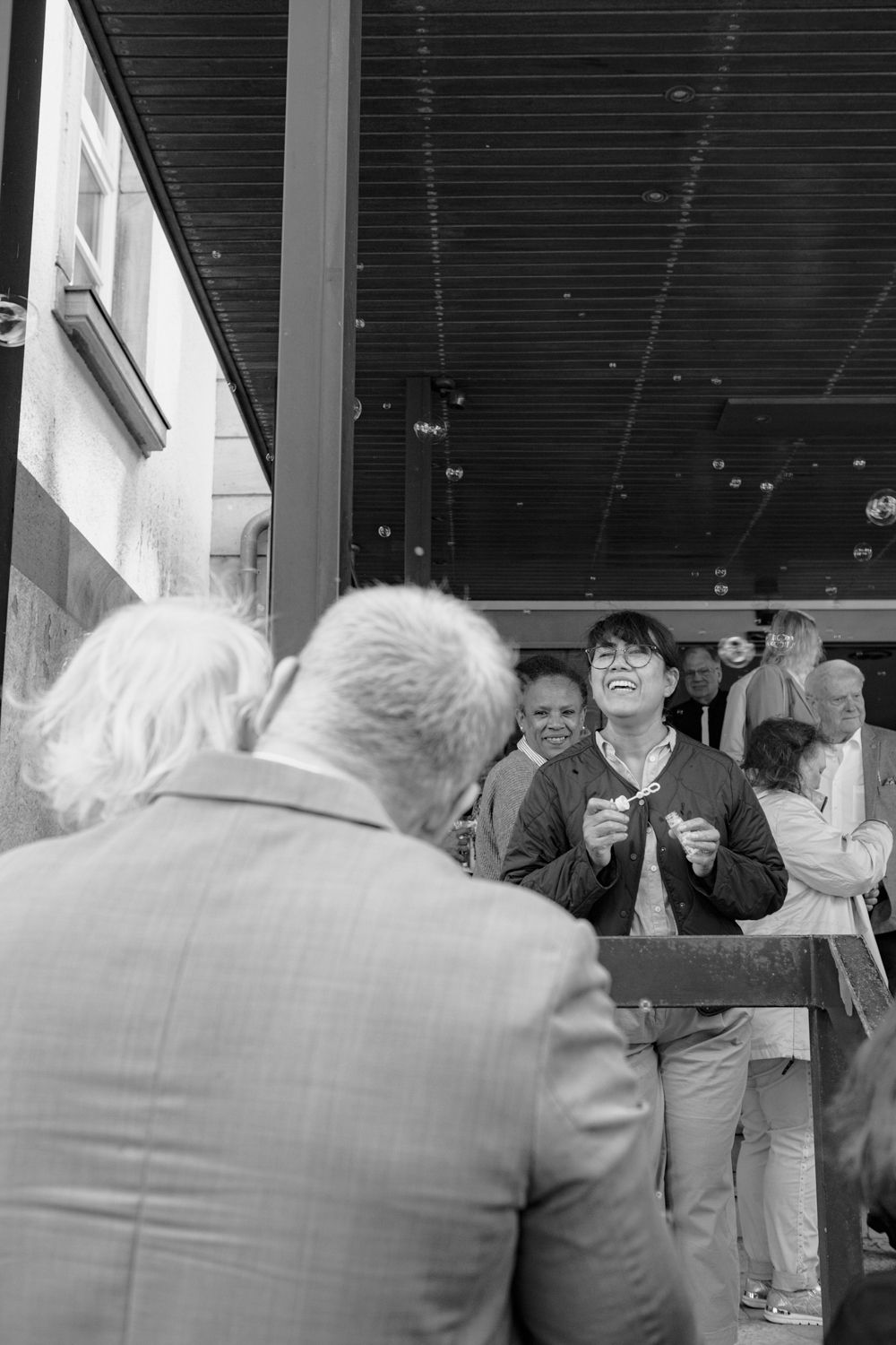 Black and white candid photo of people conversing and laughing at a social gathering indoors.