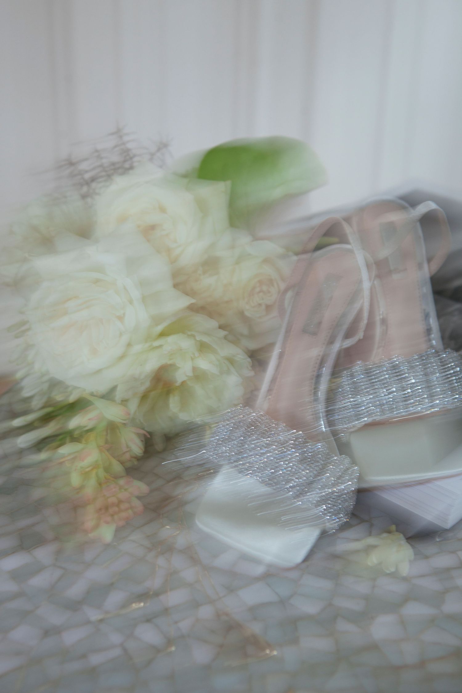 Dreamy soft-focus image of wedding shoes and white roses on a textured surface.