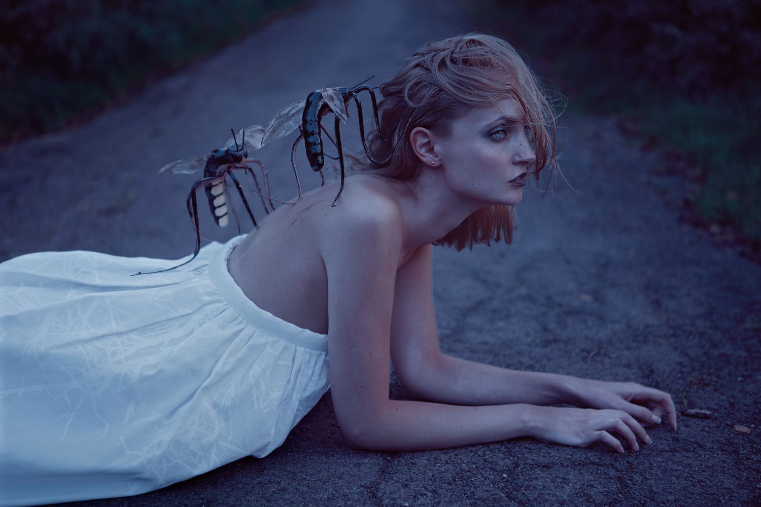 Ethereal portrait in white dress with spider-like hair accessories on dark path.