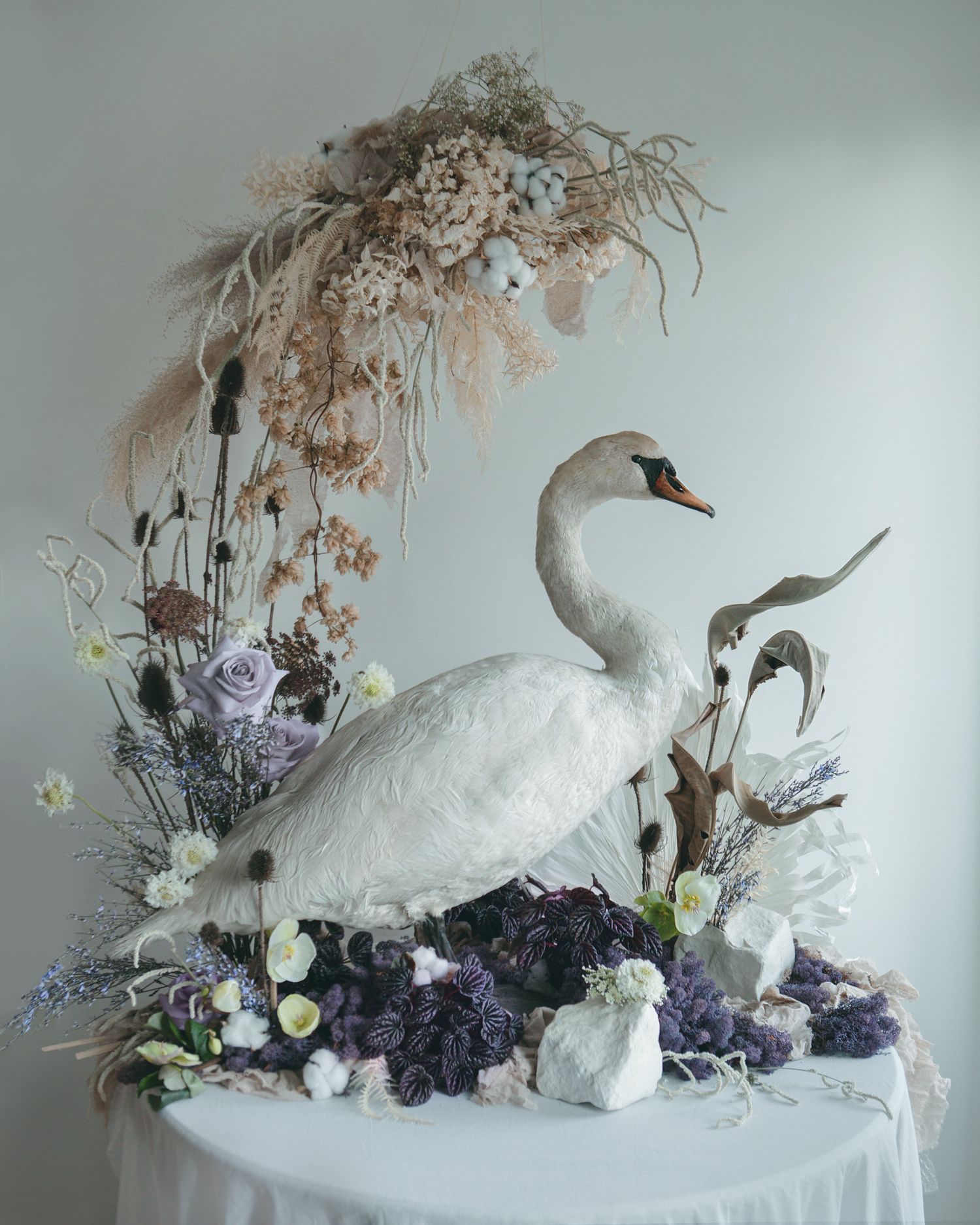 Stunning white swan taxidermy display adorned with dried flowers and purple hydrangeas on a white table.