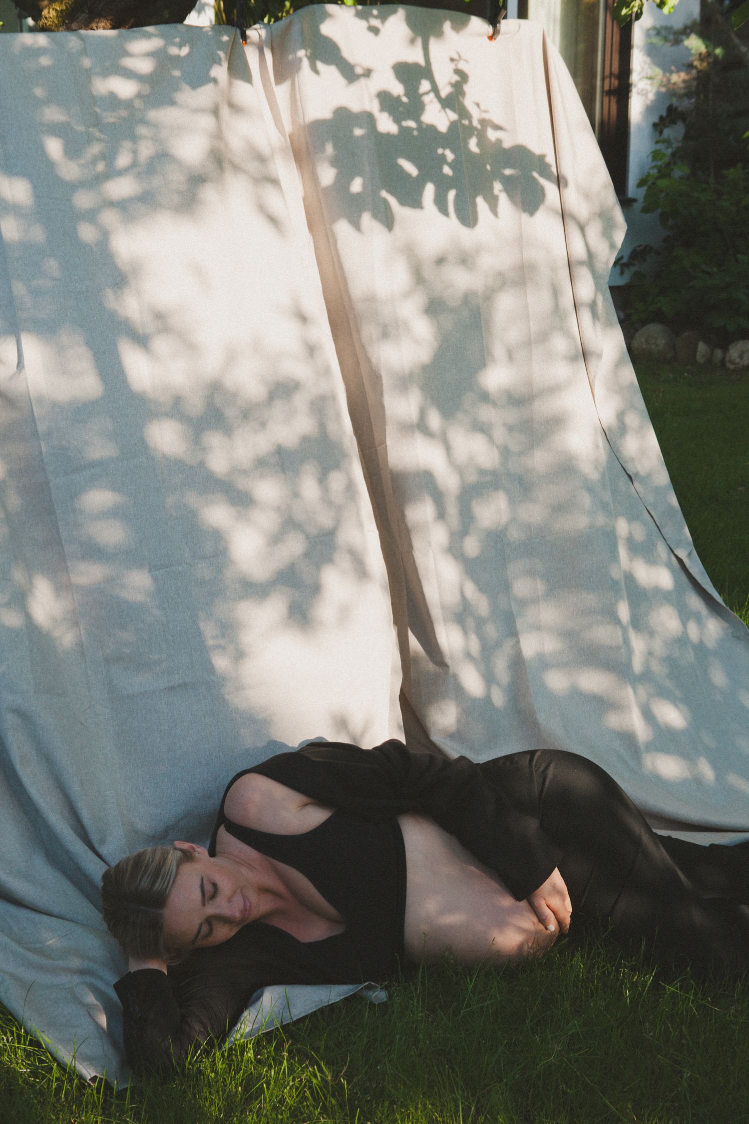 Person lying on grass with dappled sunlight and shadows creating a dreamy outdoor scene.