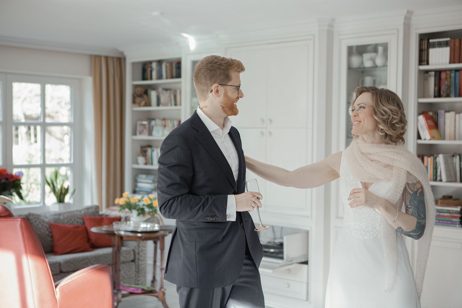 A couple shares their first look moment before their wedding in a bright living room with built-in bookshelves.