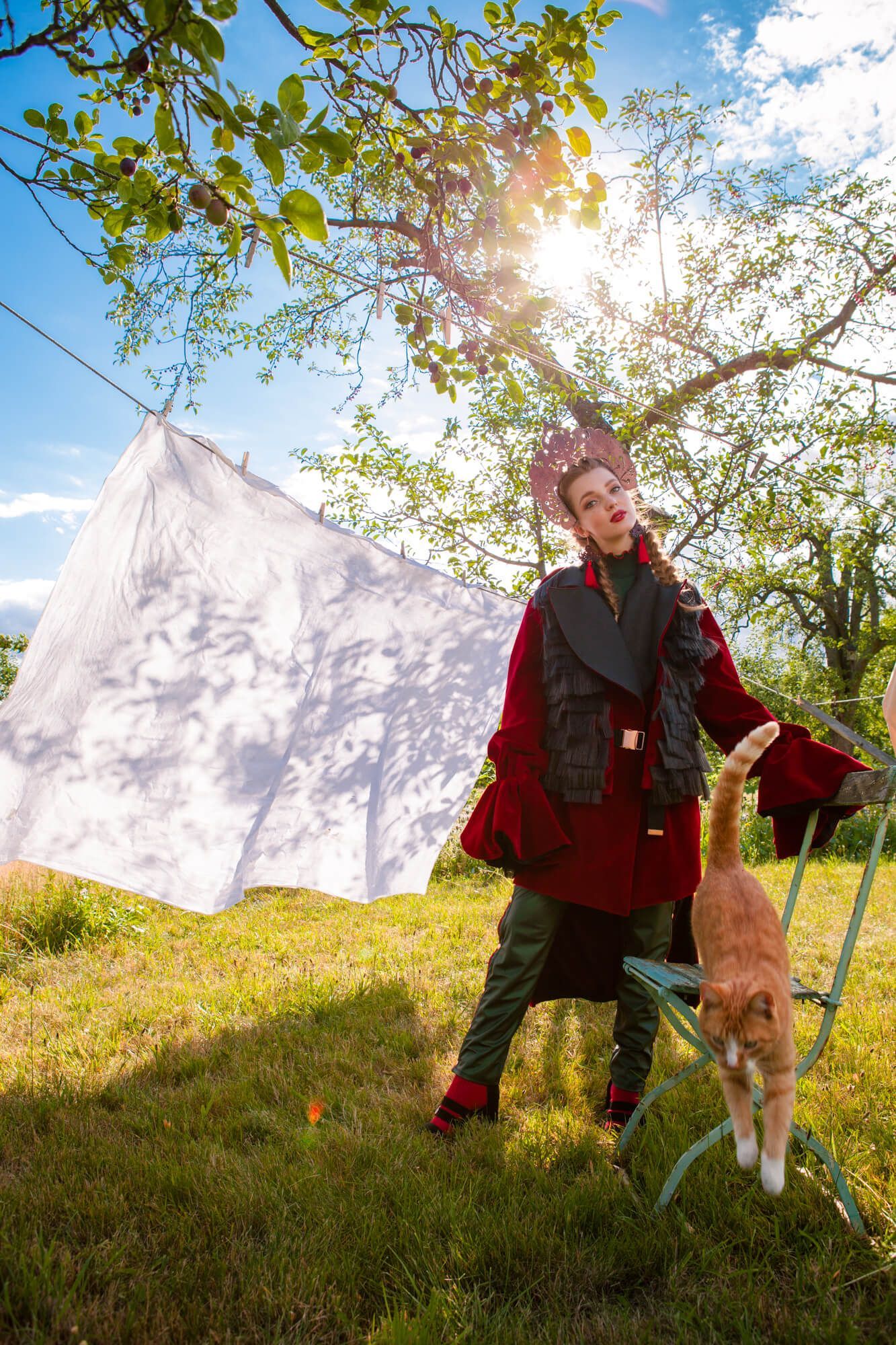 Sunny outdoor fashion scene with red coat and playful cat next to hanging laundry.