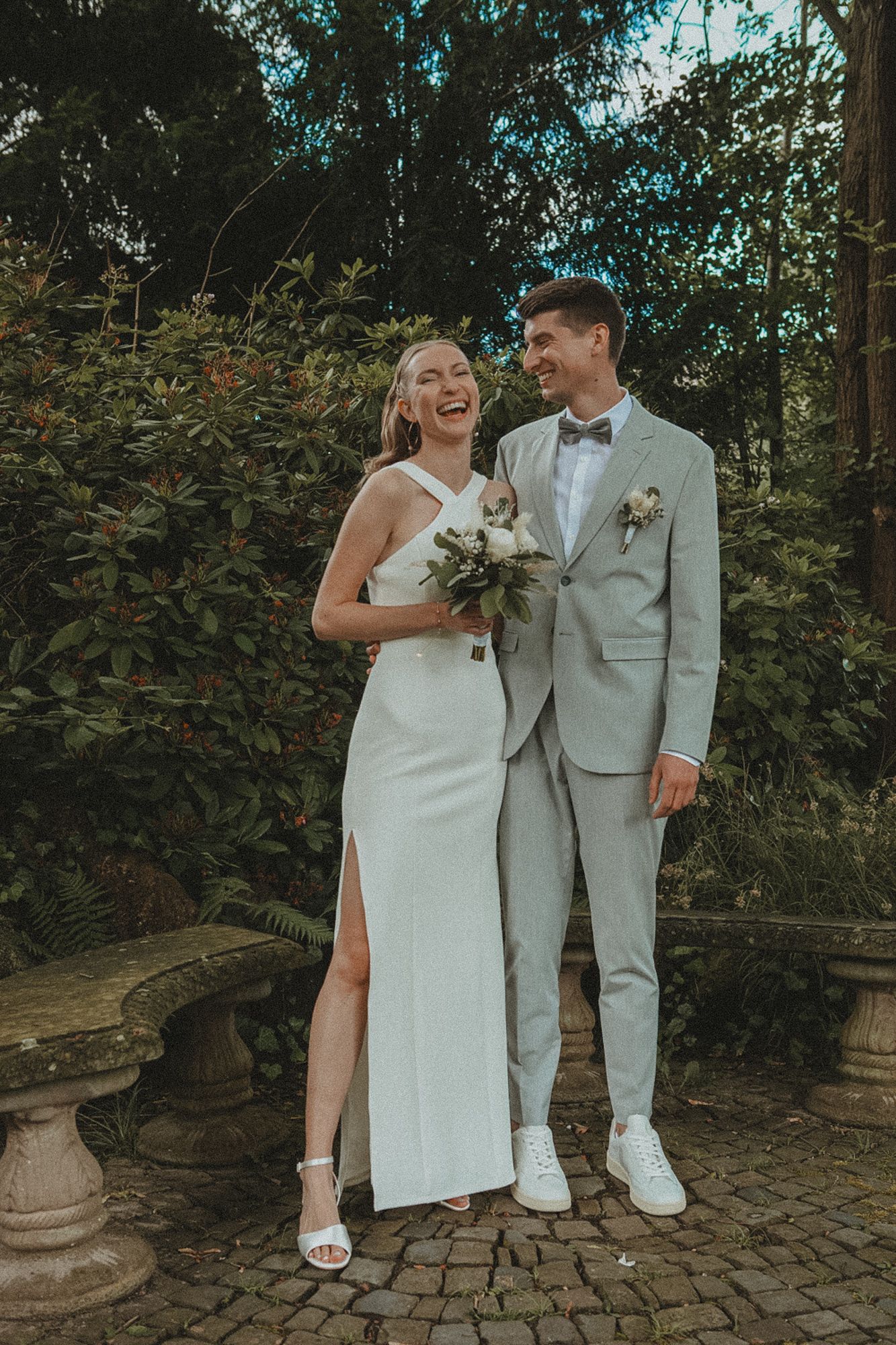 A couple in white attire share intimate moments during their outdoor wedding photoshoot on a stone patio.