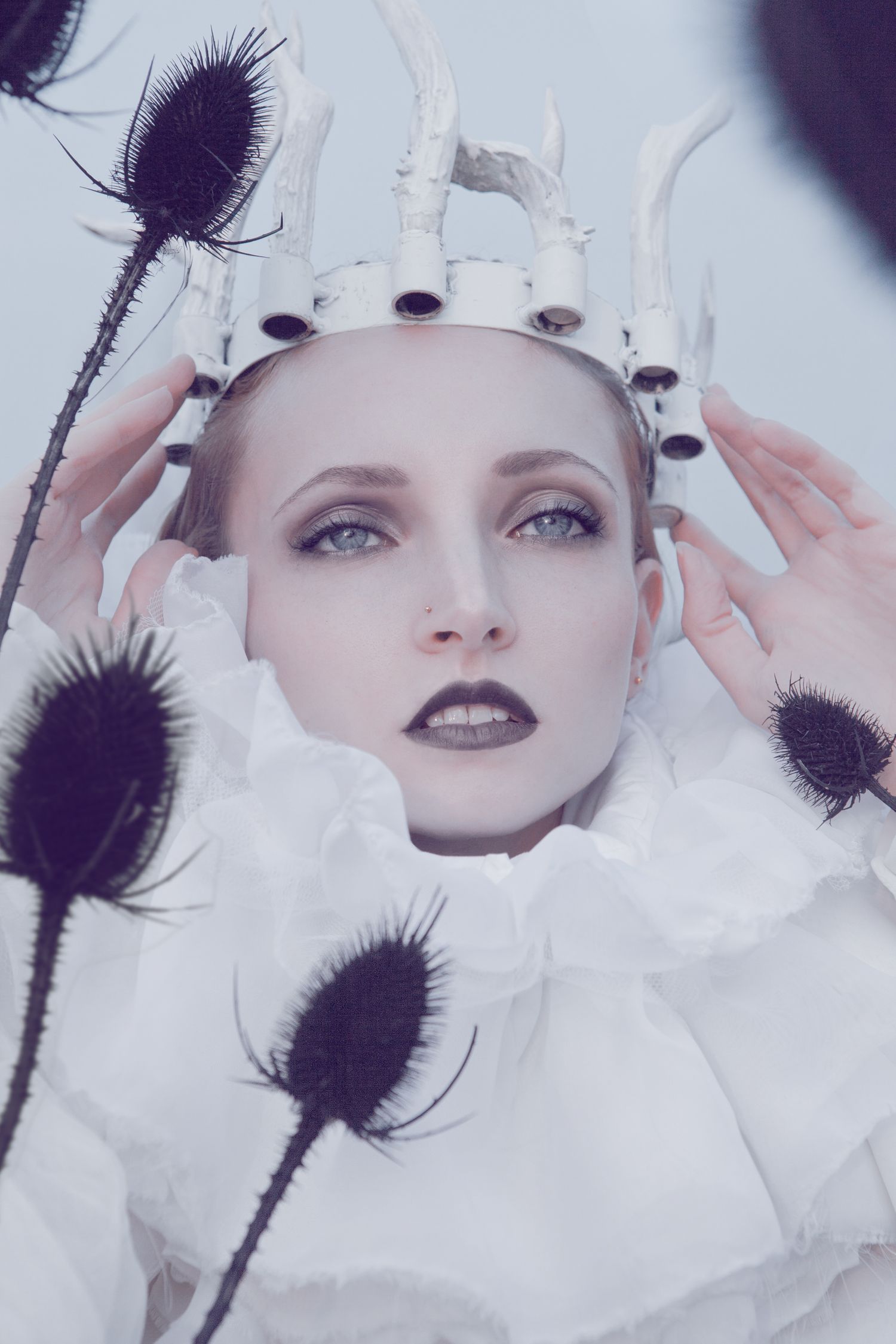 Portrait surrounded by dark thistles wearing a white crown and dramatic makeup.
