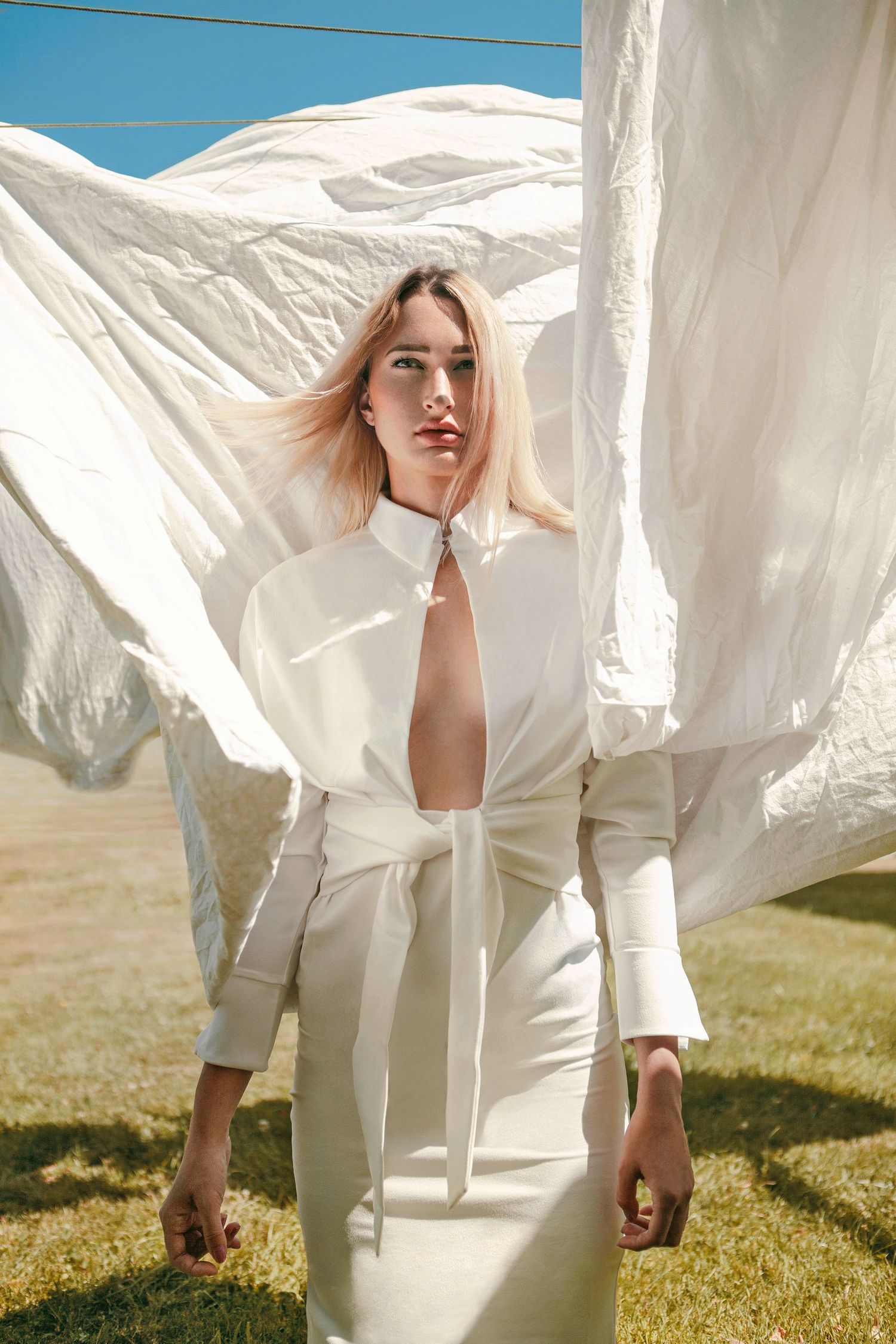 Fashion shot with flowing white fabric and structured dress in outdoor sunlit setting.