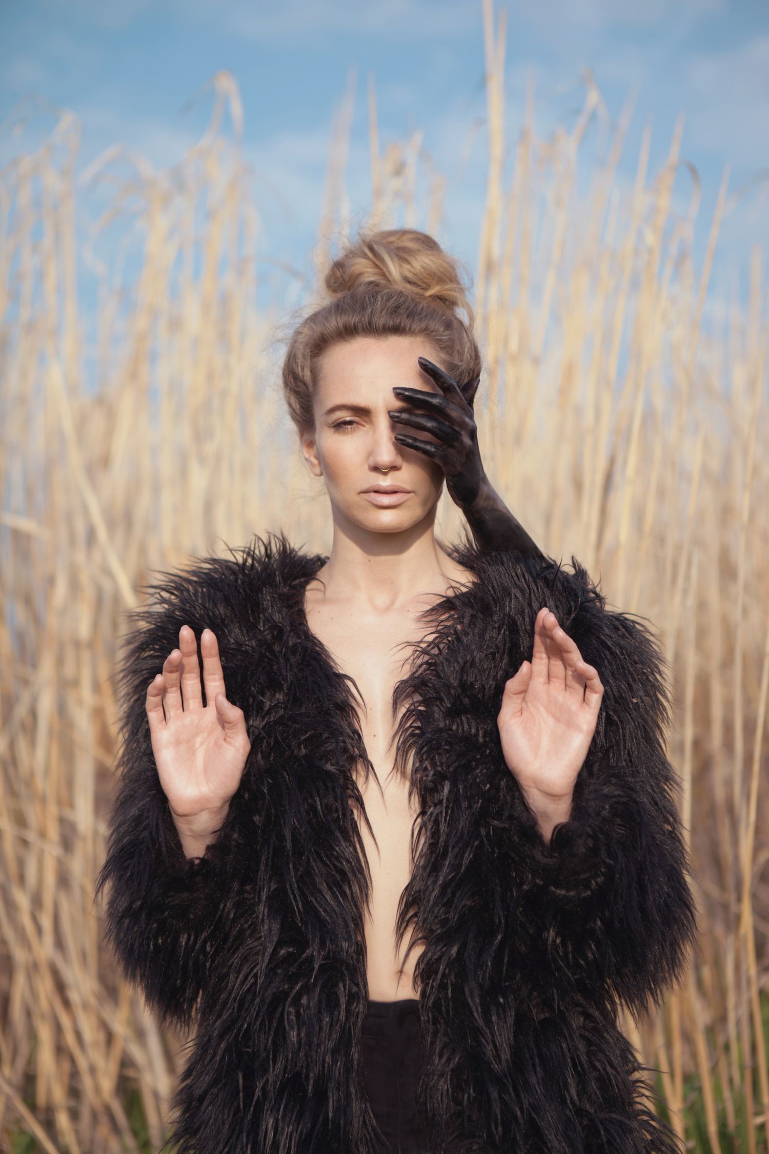 Ethereal portrait with black fur coat against golden reeds and blue sky.